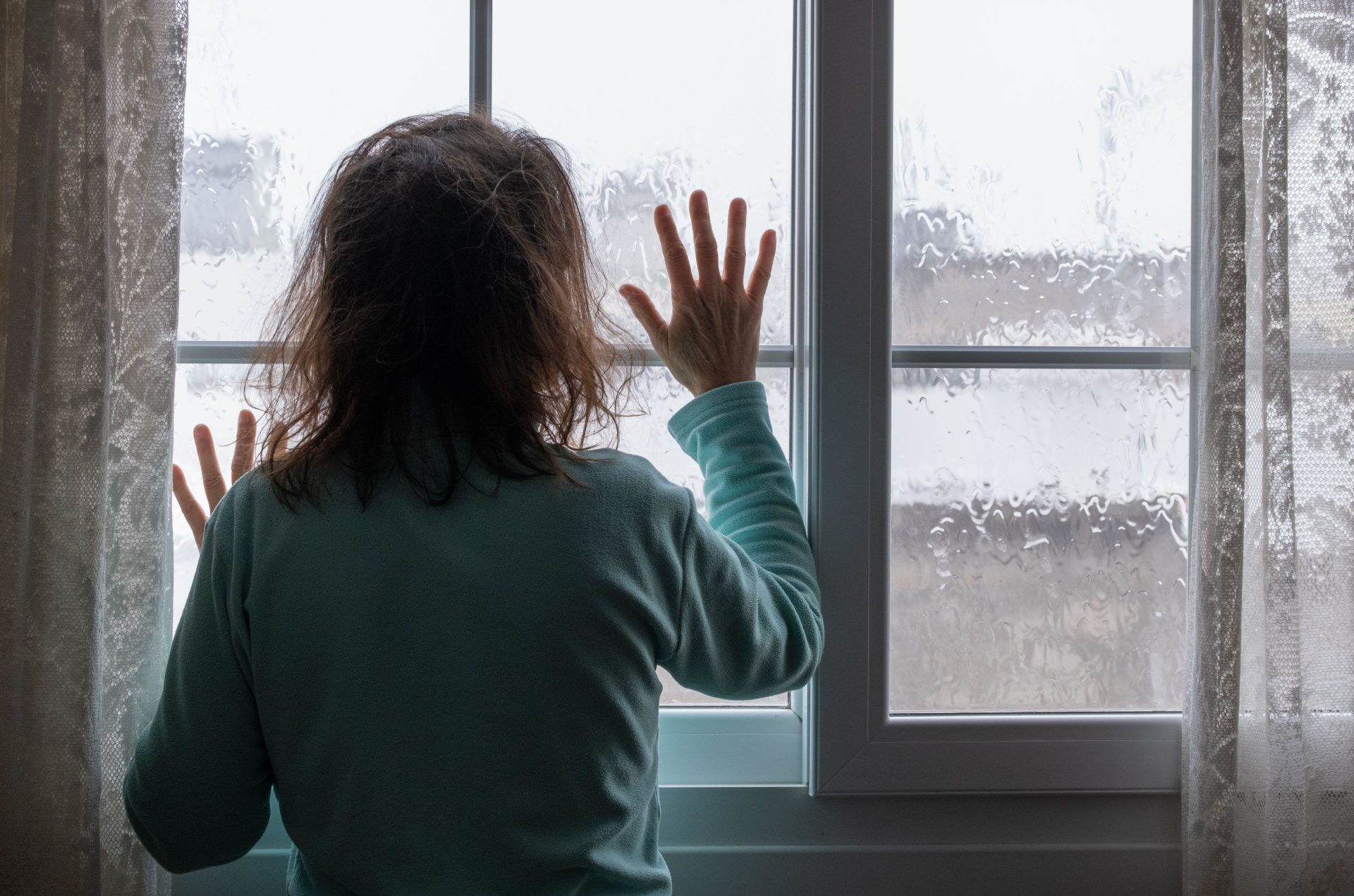 Woman looking out of window on rainy day. Conept image; female depression, domestic abuse, human trafficking, domestic violence, mental health...