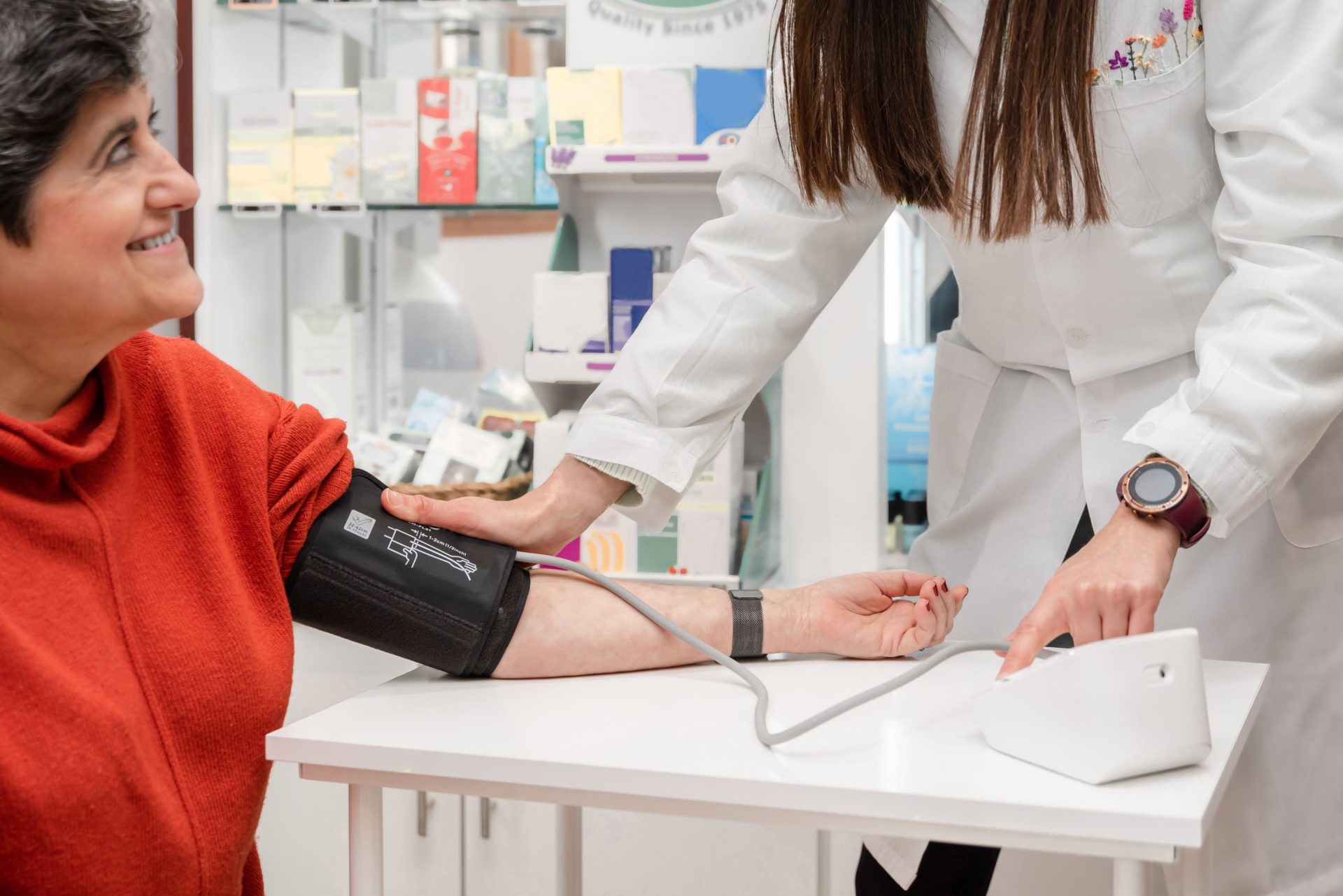 Female pharmacist in white robe using sphygmomanometer while measuring blood pressure female customer in pharmacy 