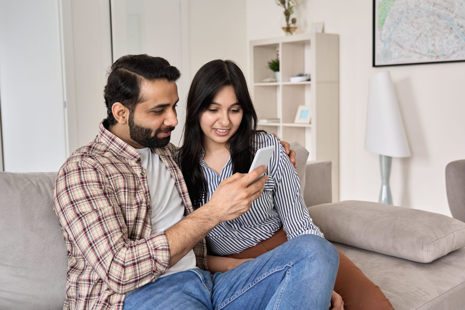 Young couple using phone sitting on sofa together at home 