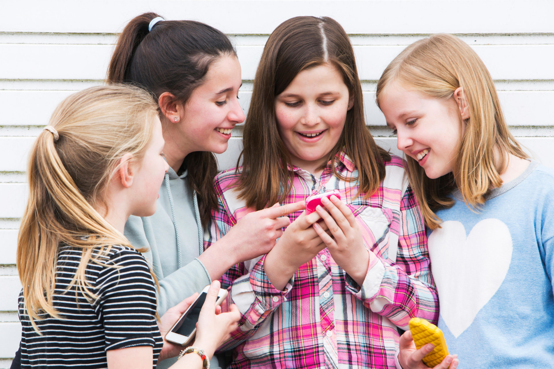 A group of four young girls looking at something on a smartphone. 