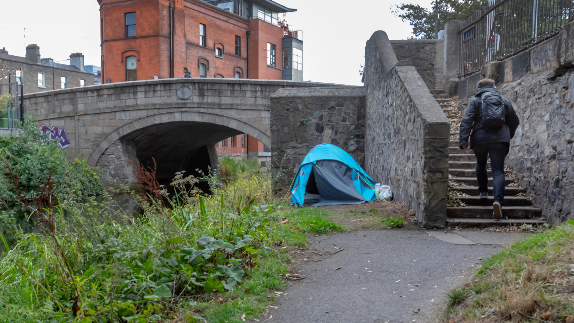 RBJ9KR A tent for someone homeless and a man walking by the Grand Canal waterway in Dublin, Ireland.