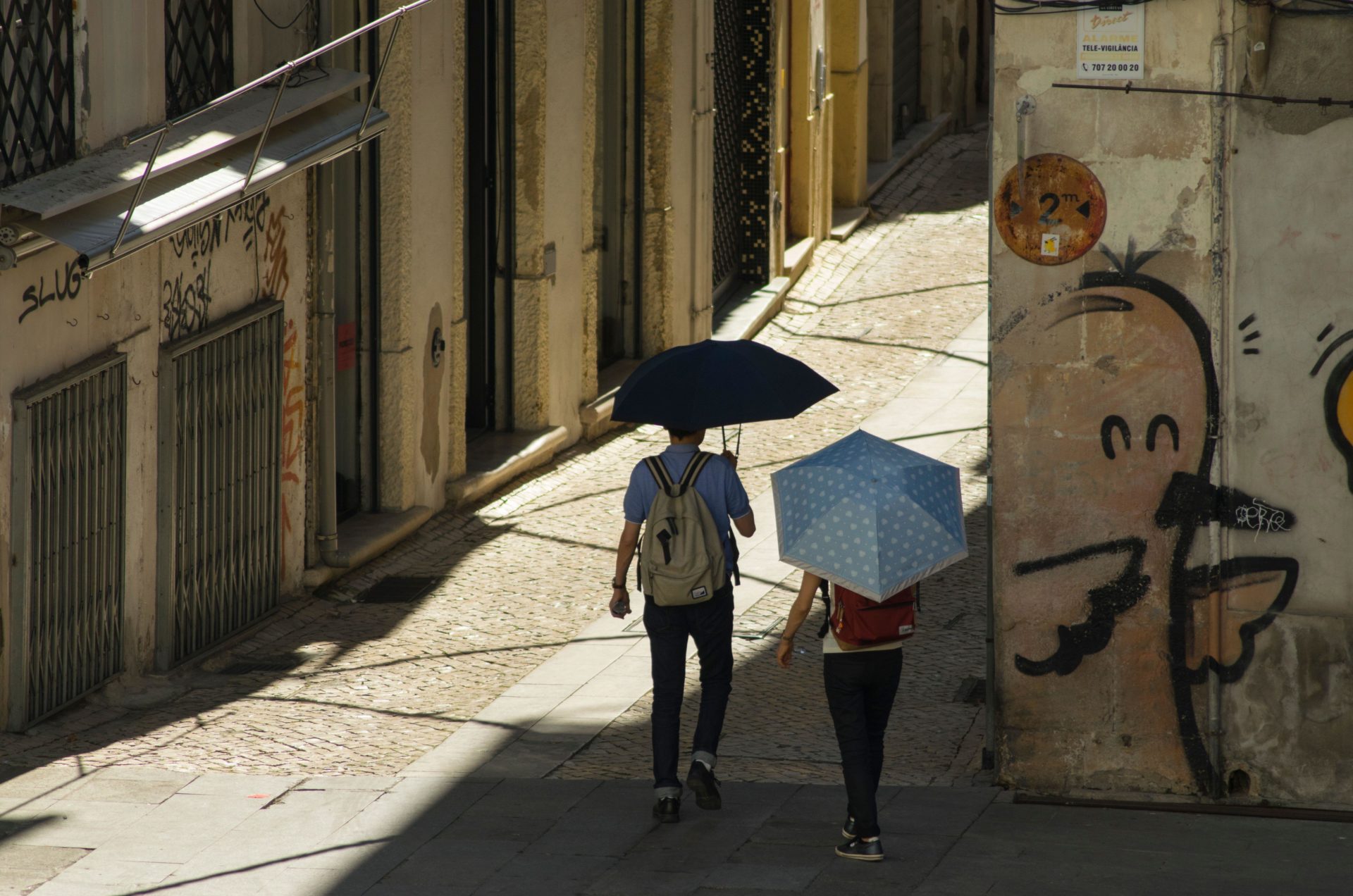 People try to keep cool during a heatwave in Coimbra Portugal, using umbrellas to find shade from the sun.