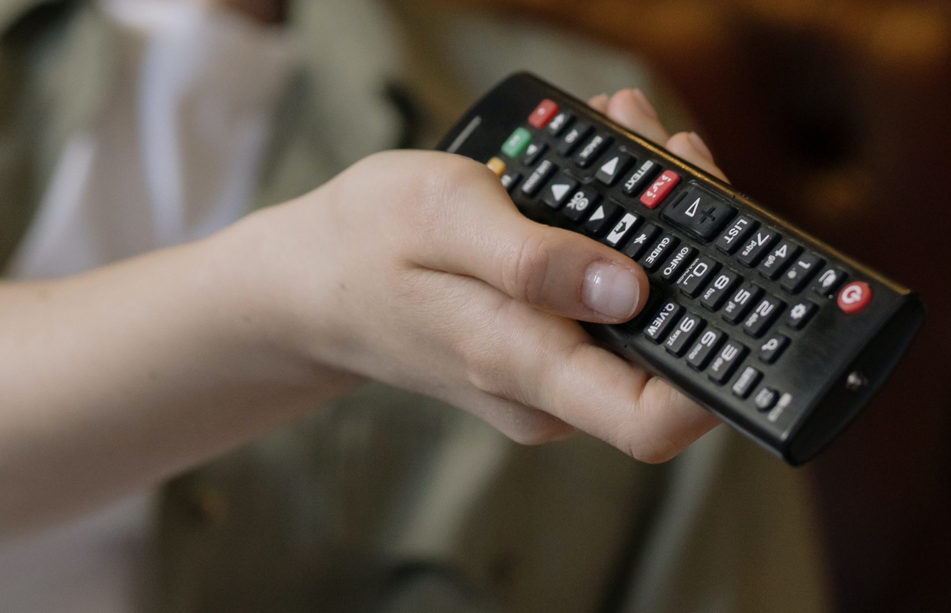 Person holding a TV remote, pointing it at a television.