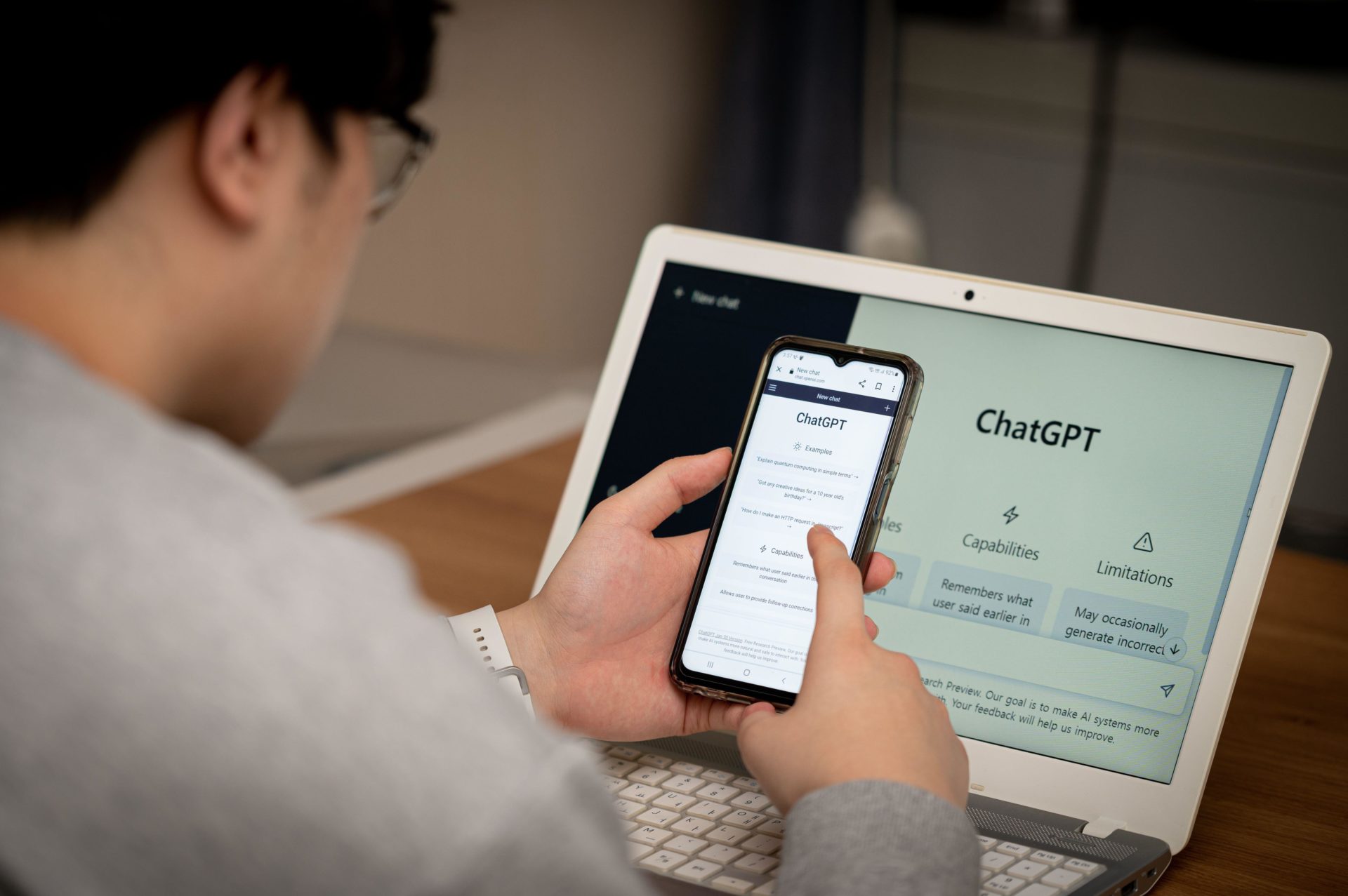 A young man using ChatGPT on his phone and laptop.