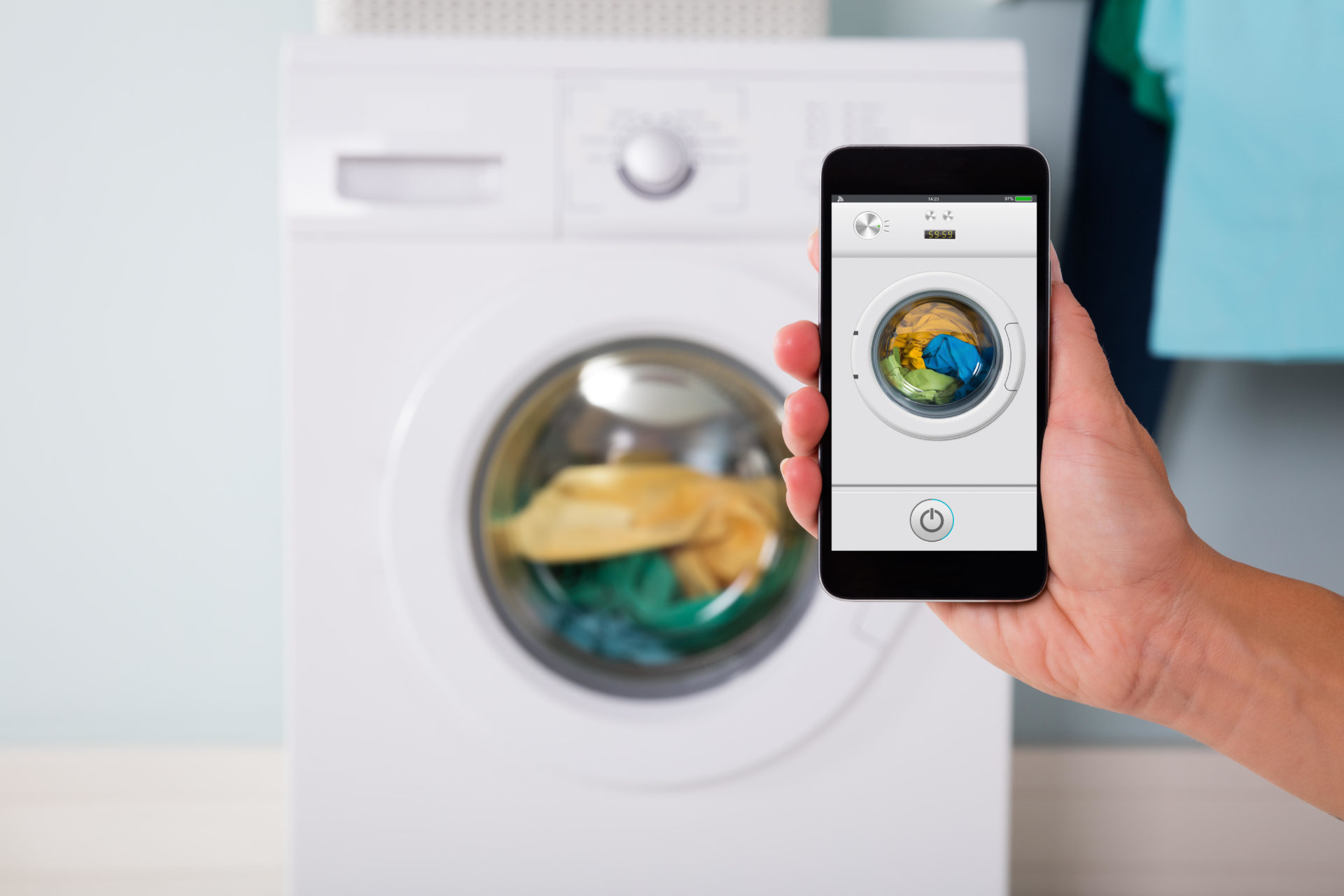 Close-up of person hand operating smart washing machine using mobile phone app. Image: Andriy Popov / Alamy Stock Photo 