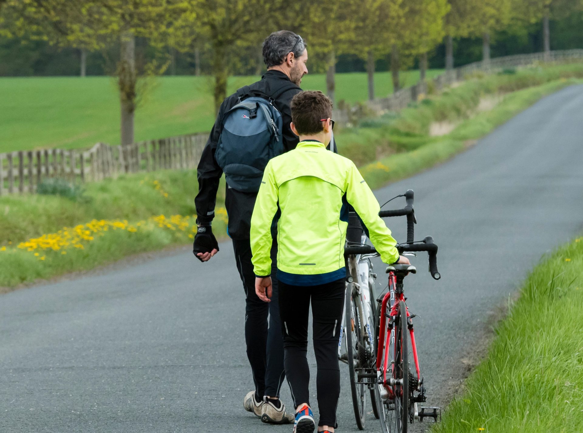 A father and son push their bikes along a scenic country lane