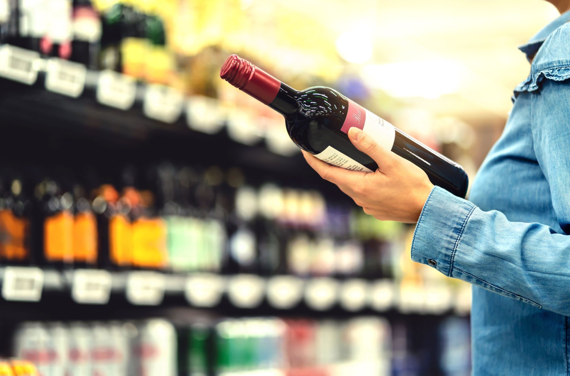 2B8C6R4 Alcohol shelf in liquor store or supermarket. Woman buying a bottle of red wine and looking at alcoholic drinks in shop.