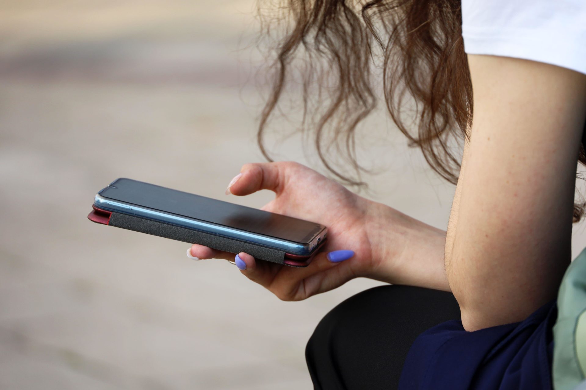 2RXCKTC Smartphone in female hands close up. Girl using mobile phone while sitting on city street