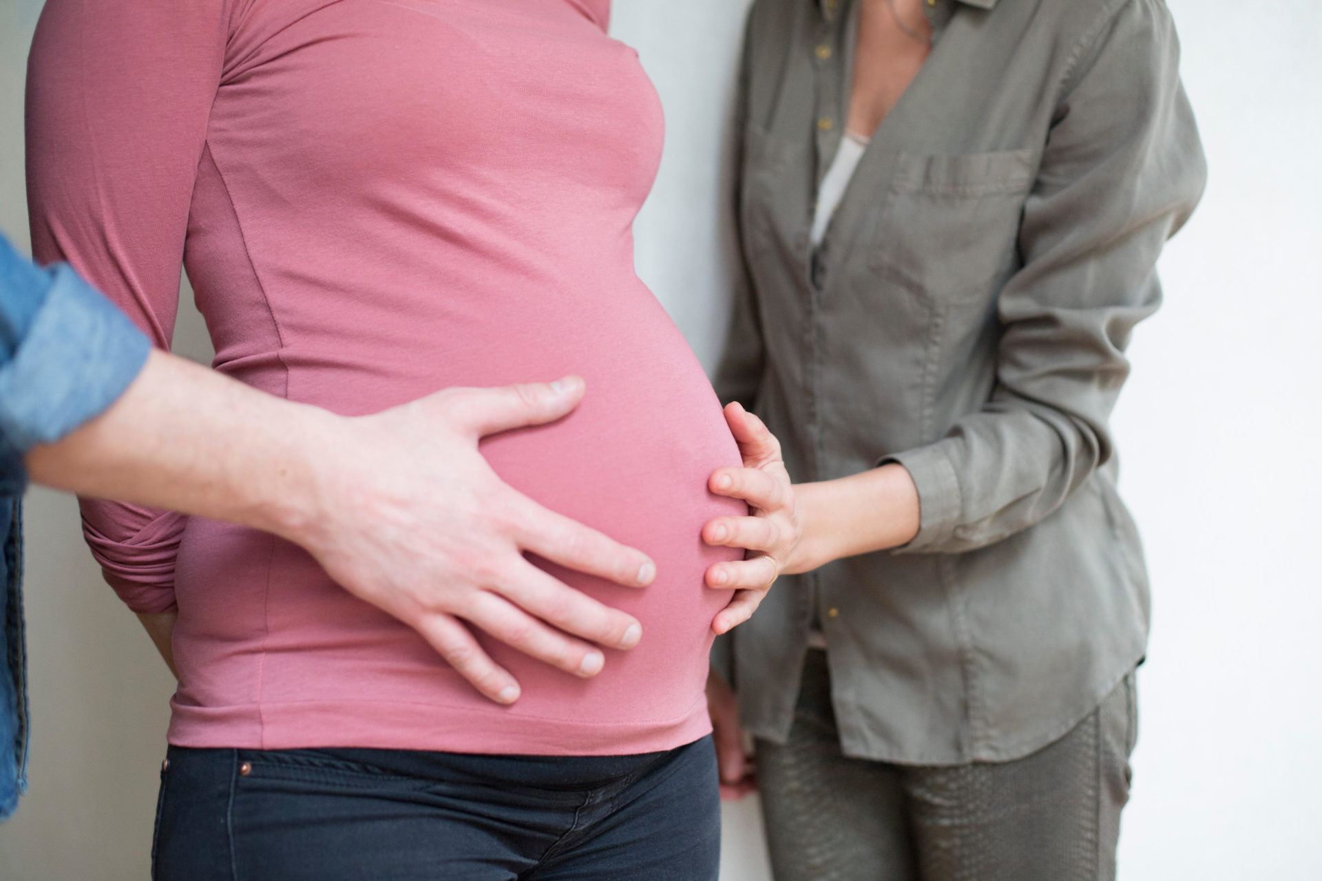 Close up of a couple touching the stomach of a pregnant woman as they are having a child through surrogacy.