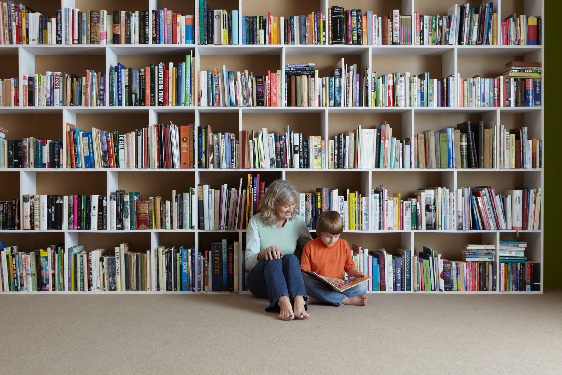 An adult and child reading by a bookshelf