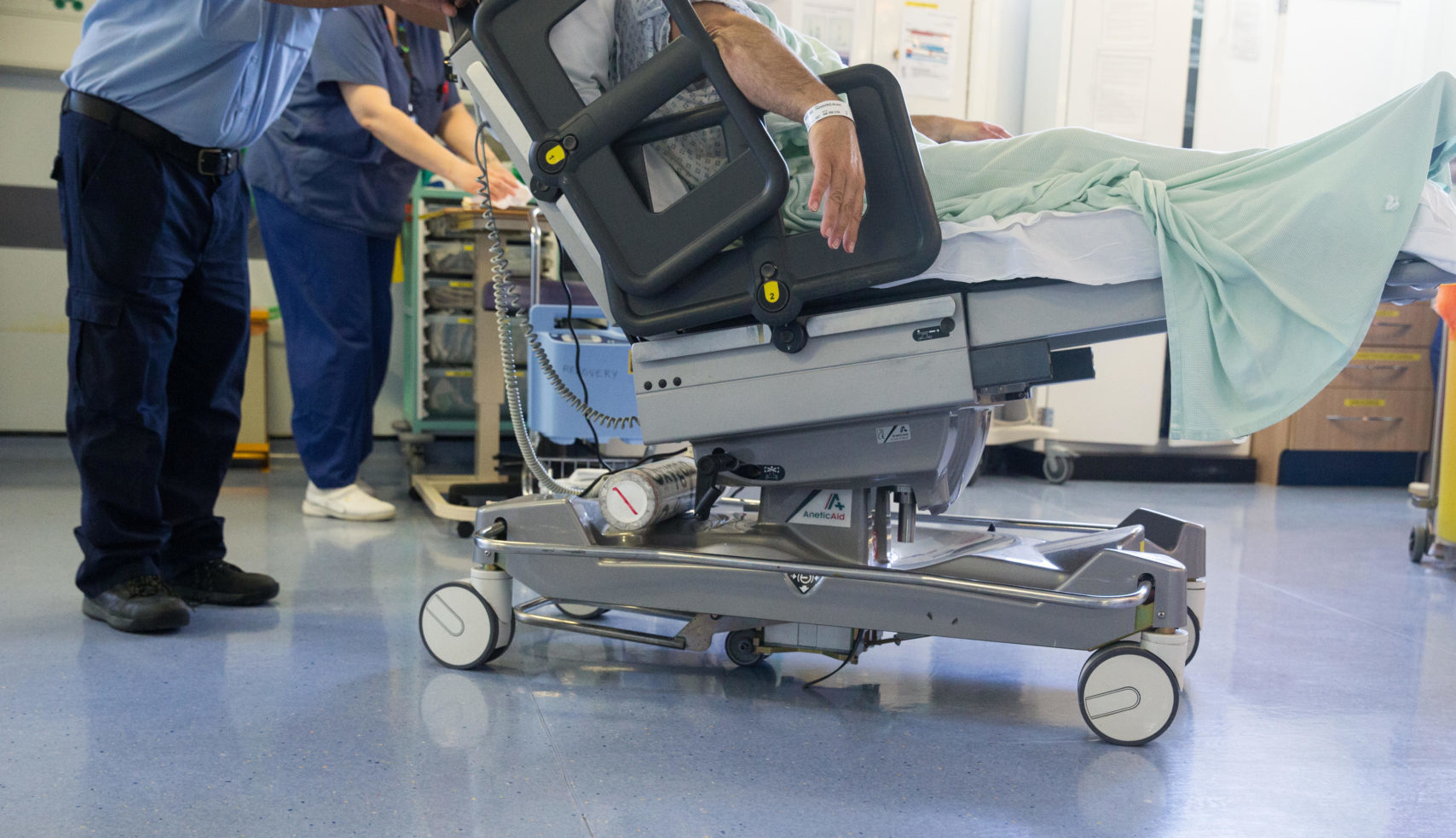 A hospital worker wheels a patient on a trolley through a ward after an NHS operation