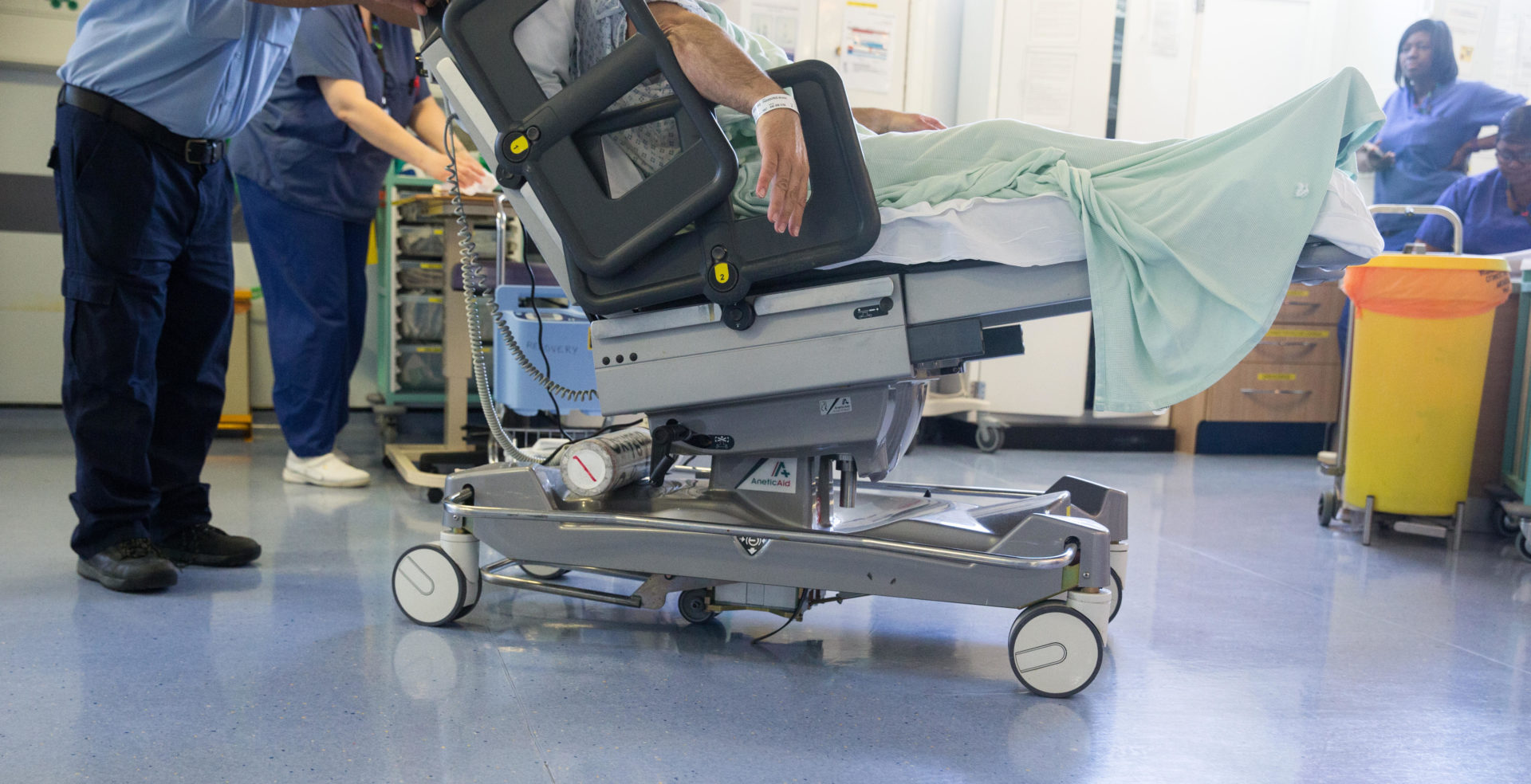 A hospital worker wheels a patient on a trolley through a ward after an NHS operation
