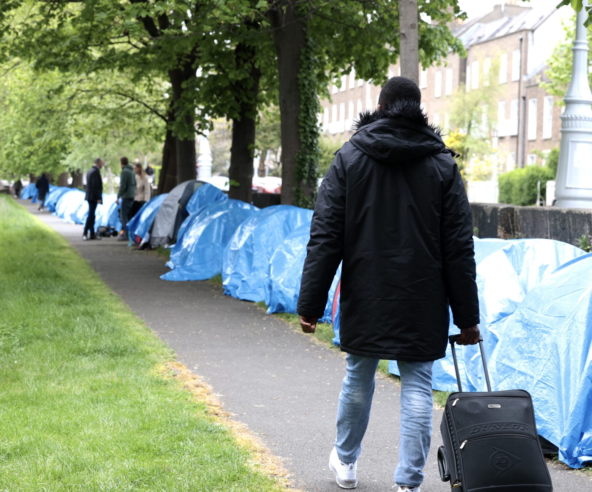 People with suitcases walking by asylum seekers tents along the Grand Canal in Dublin, 4-5-24.
