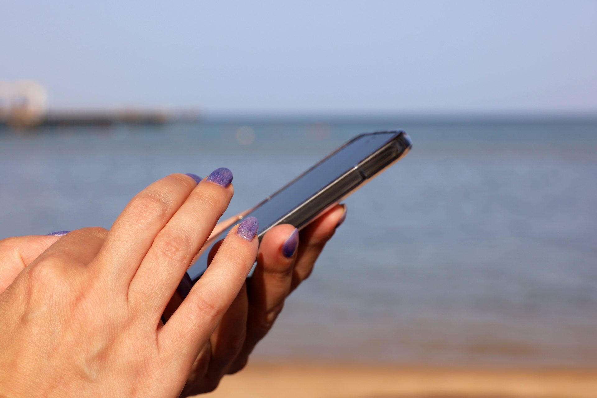 Woman holding phone on beach, using data. Image: Oleg Elkov / Alamy Stock Photo