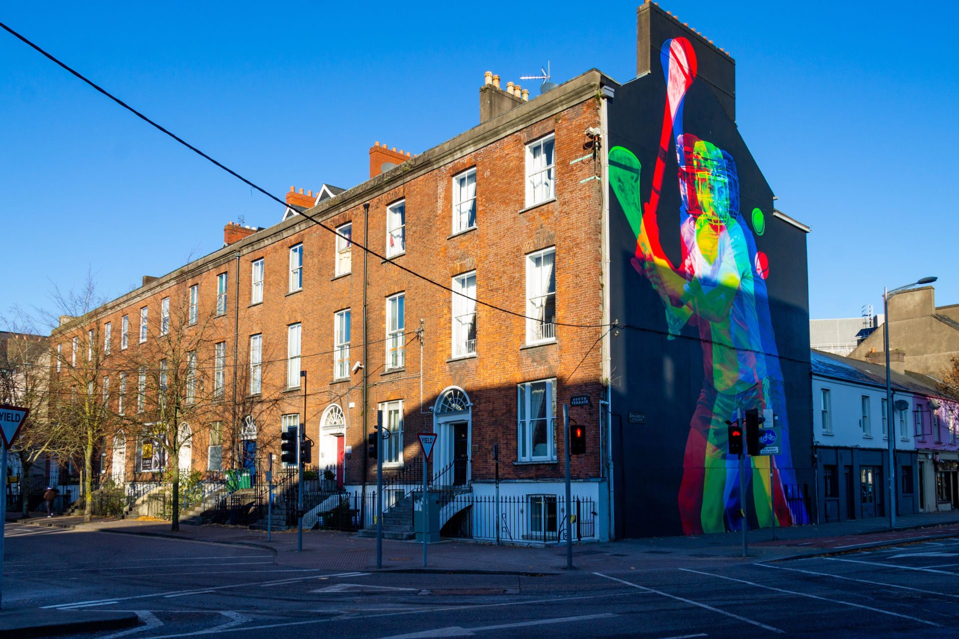 Row of terraced houses in Cork City Ireland with mural of man hurling on gable end.