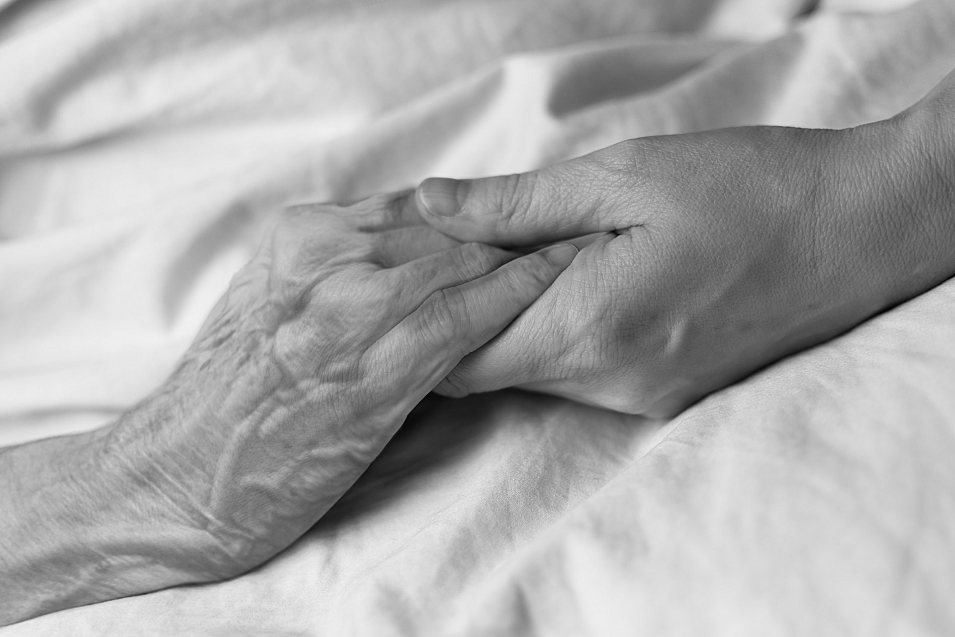 A young woman holding the hand of an old woman in a hospital bed, in black and white.