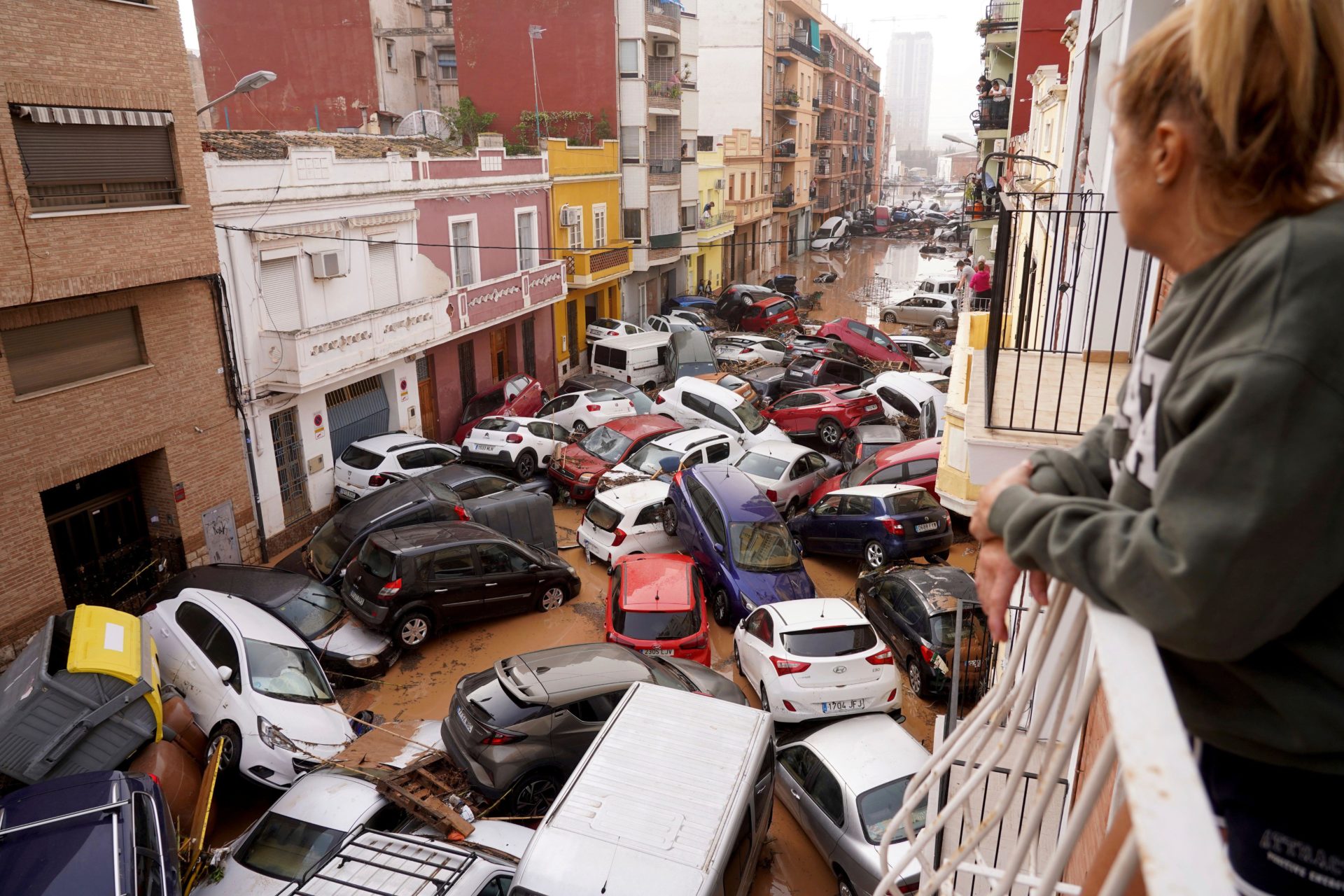 A woman looks out from her balcony as vehicles are trapped in the street during flooding in Valencia