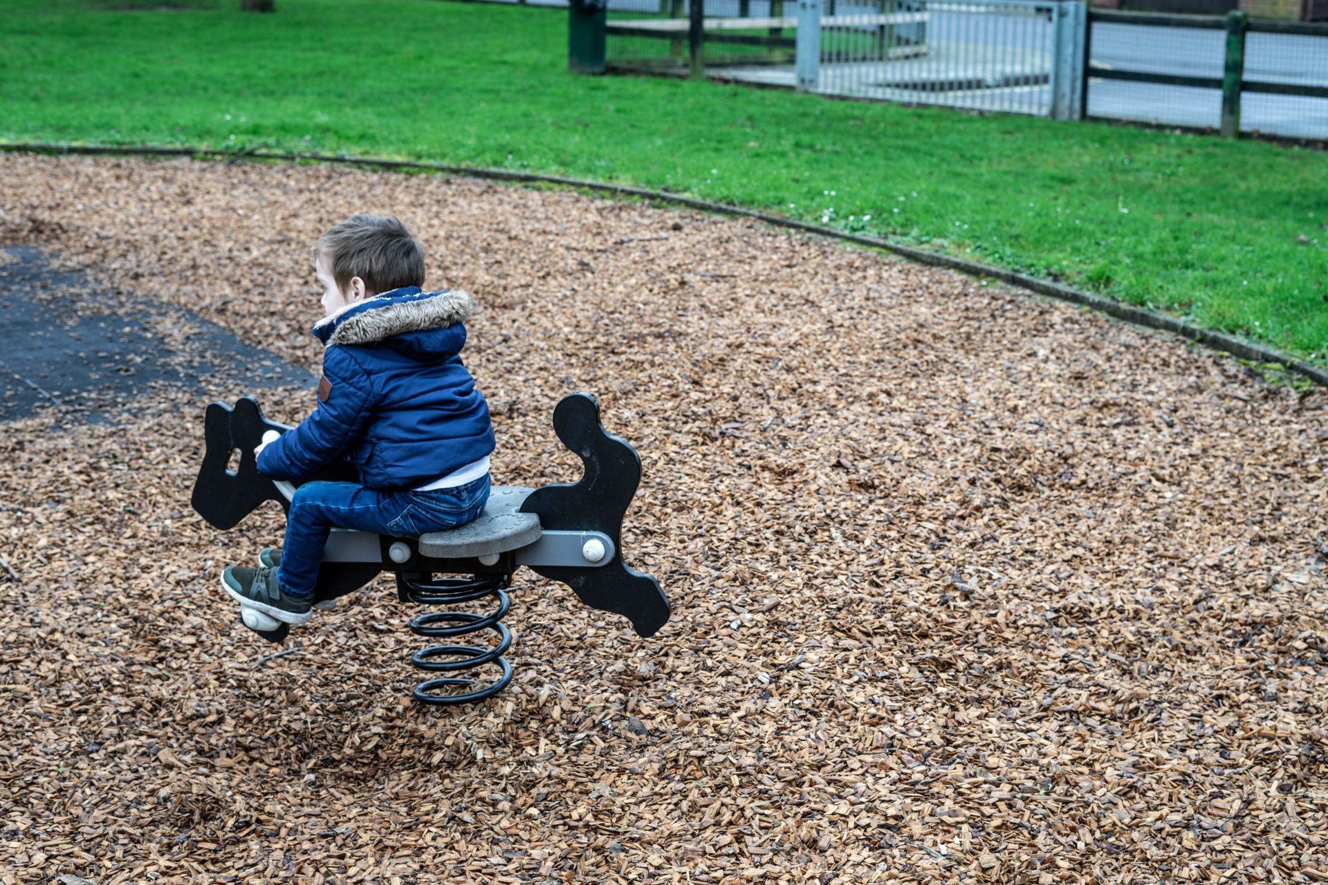 A small boy playing on a rocking ride in the park.