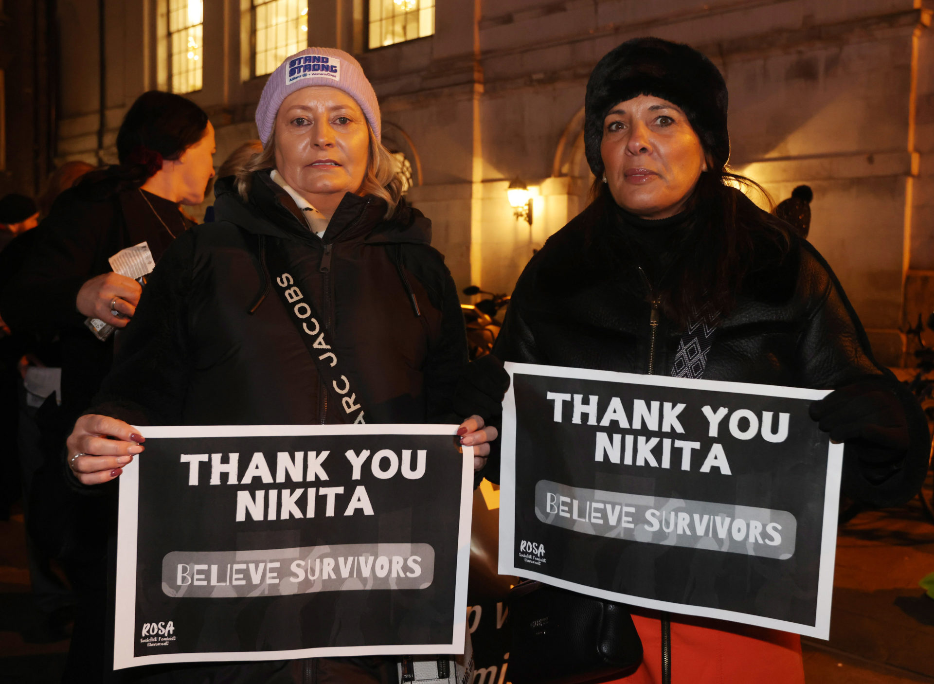 Two women at the rally for Nikita Hand in Dublin. Both are holding black signs with white text reading "Thank you Nikita. Believe survivors".