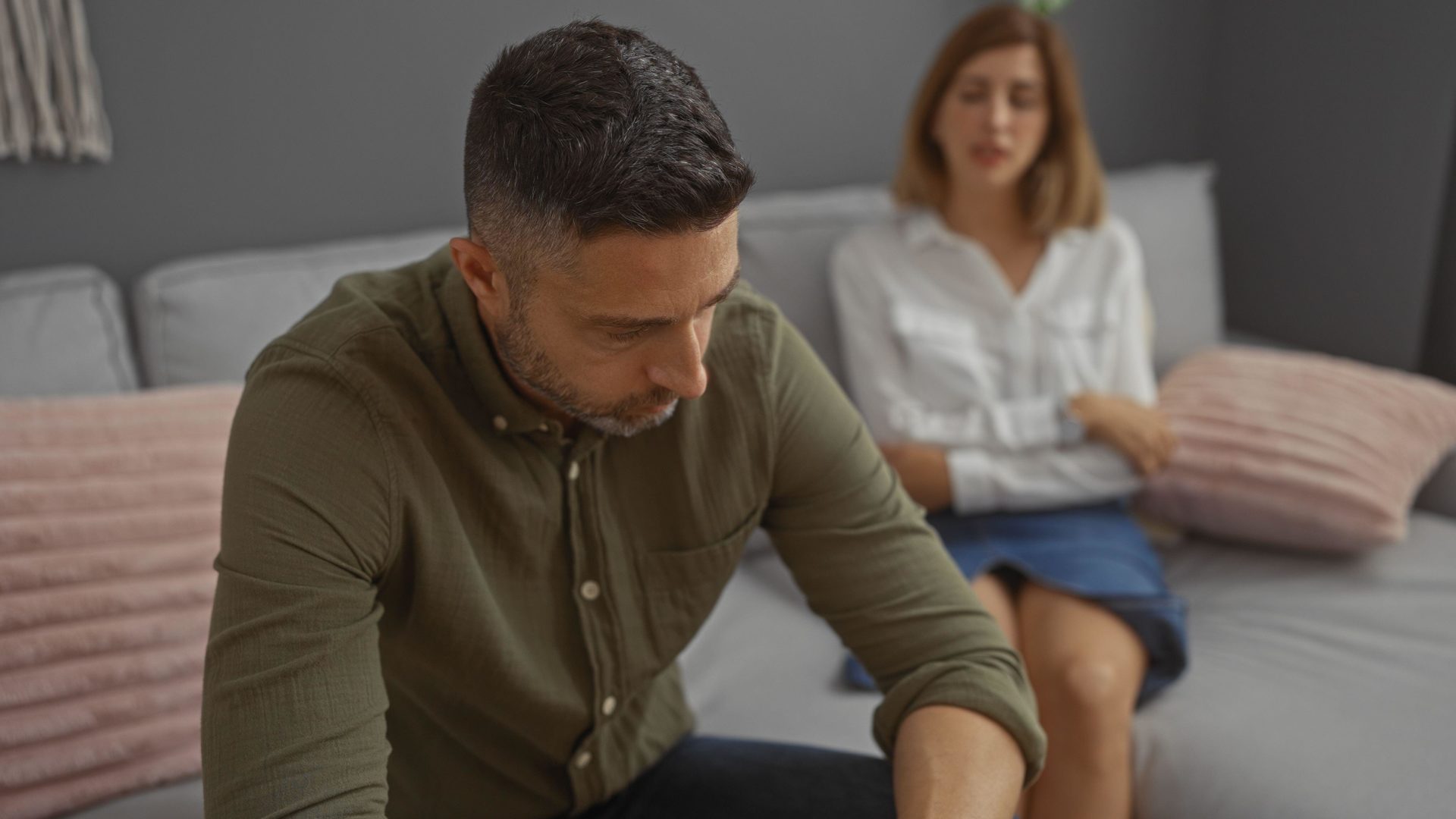 Man and woman sitting together indoors in a living room, both upset and deep in thought.