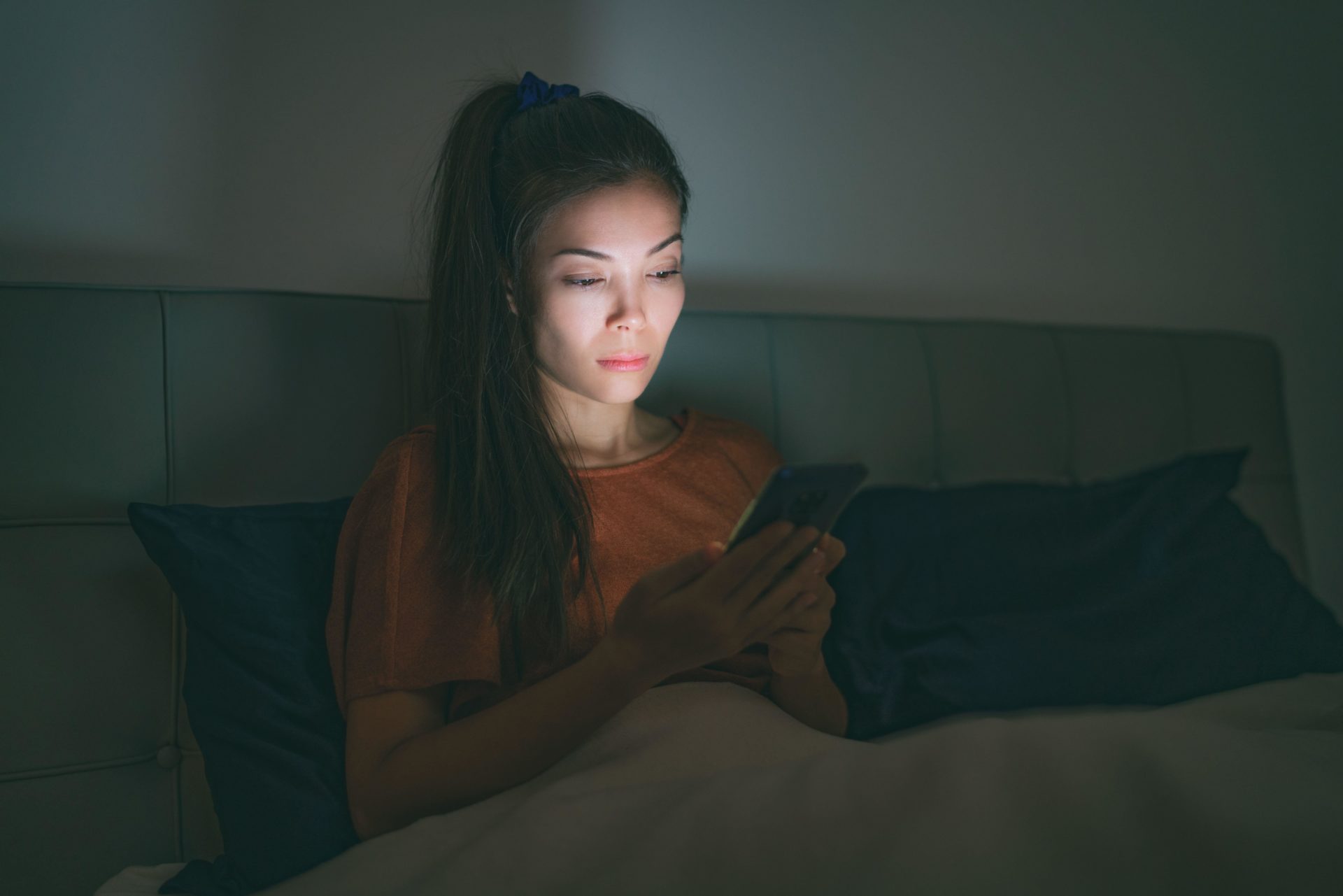 Image shows a woman looking at her phone in bed