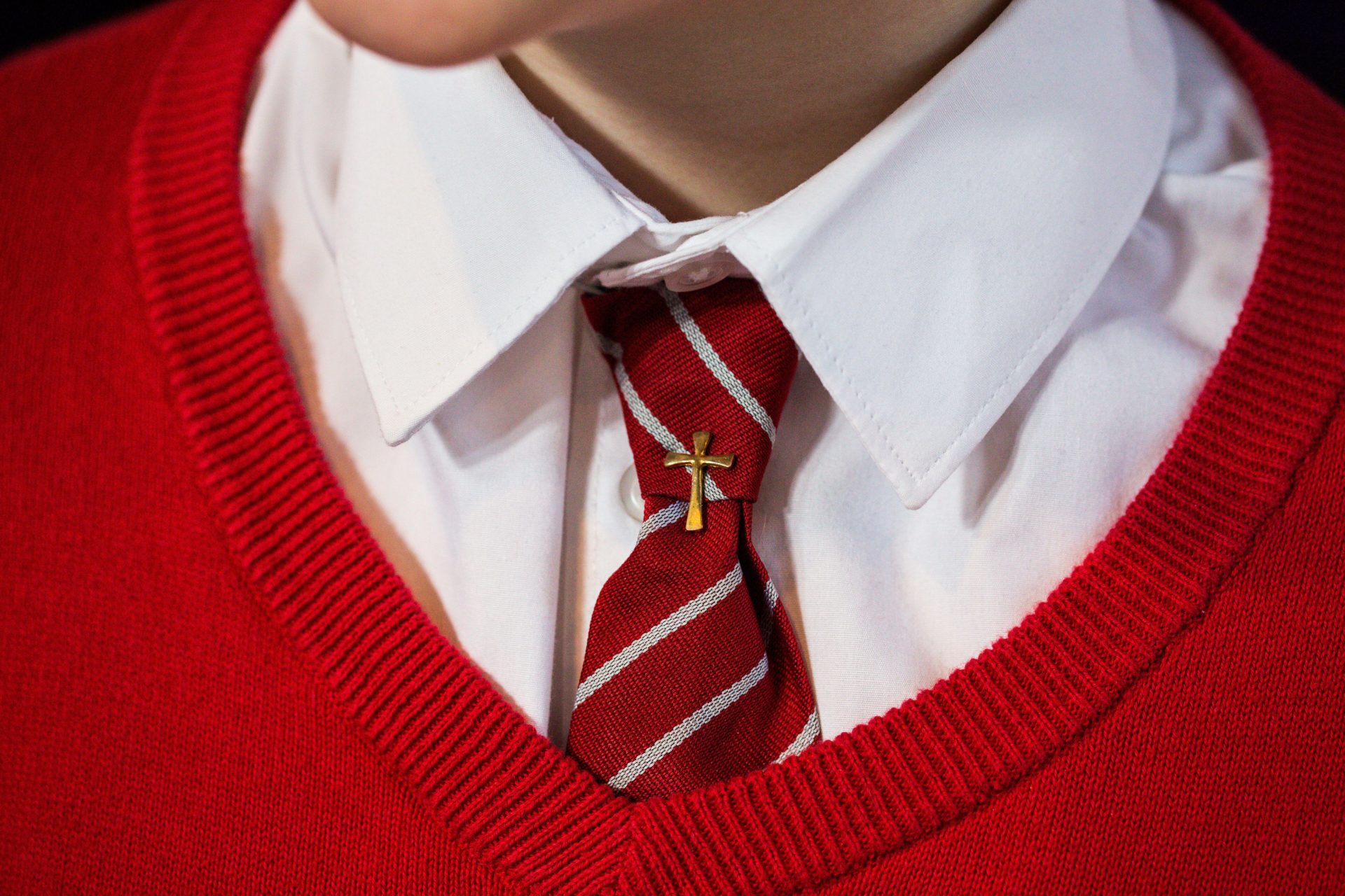 A student's red school uniform, with a gold cross pinned to the tie.