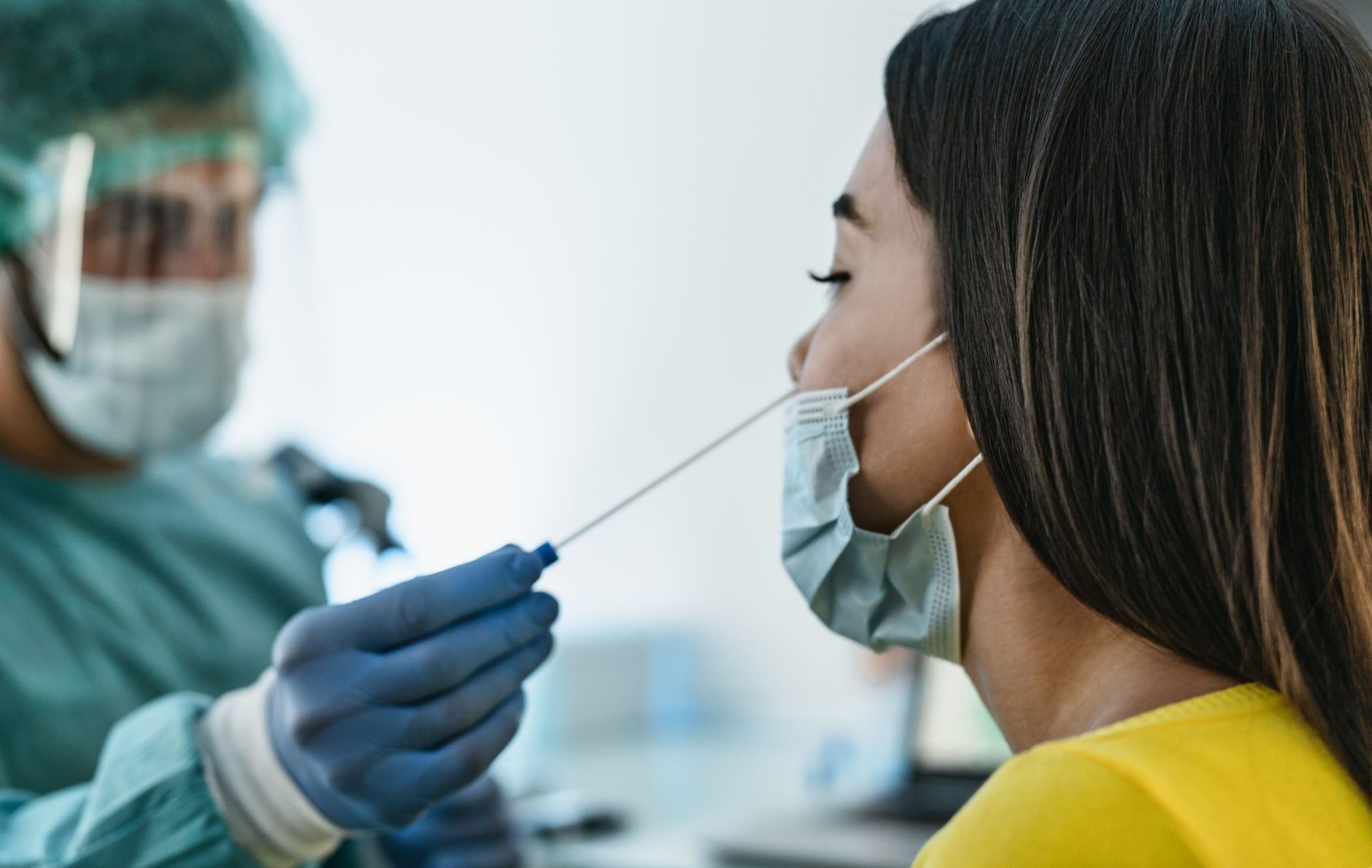 Medical worker wearing personal protective equipment doing a COVID virus swab on female patient