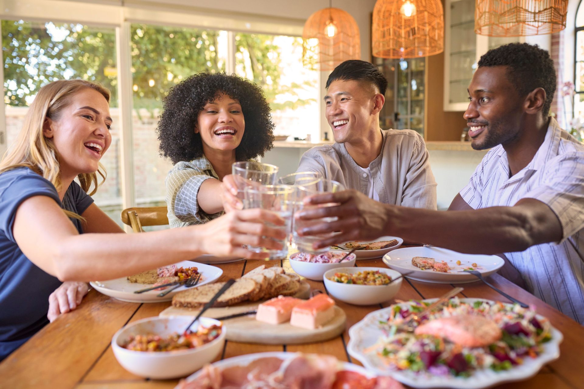 Group Of Friends Sitting Around Table Enjoying Meal At Home Making Cheers With Water