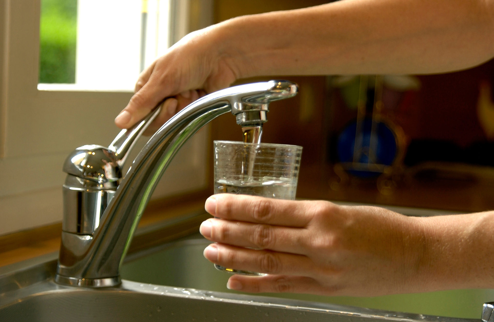 Woman filling a glass of water from the kitchen sink tap.