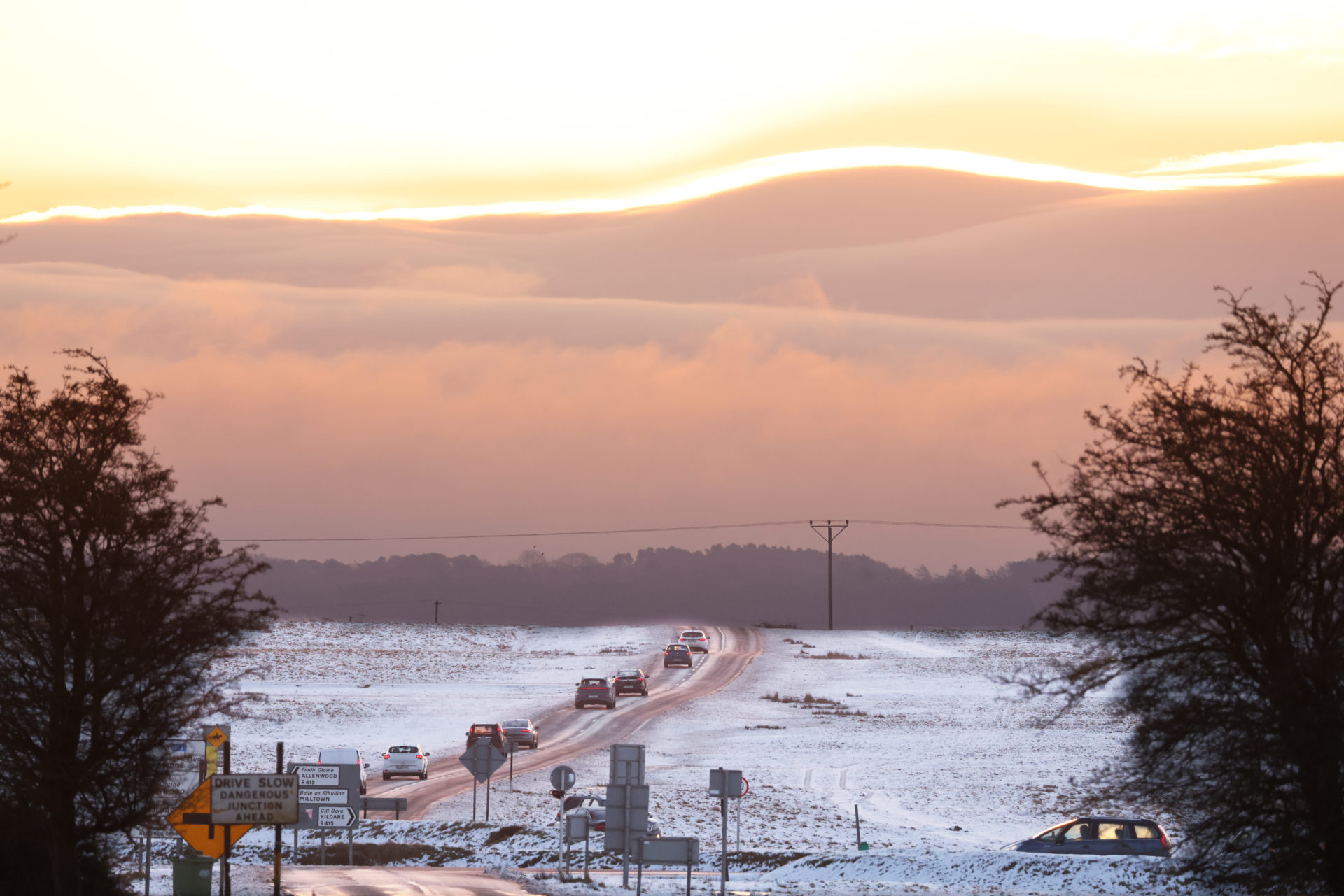 6/1/2025. Kildare, Leinster, Ireland. Commuters head across the icy roads on the snow covered Curragh Plains in County Kildare as dawn breaks. The country is facing into a week of freezing days and nights with very difficult driving conditions. Photo shows the sun about to break behind the Lug ( Lugnaquillia, Lugnaquilla ), which is Wicklow and Leinsters highest mountain. Photo: Eamonn Farrell/© RollingNews.ie