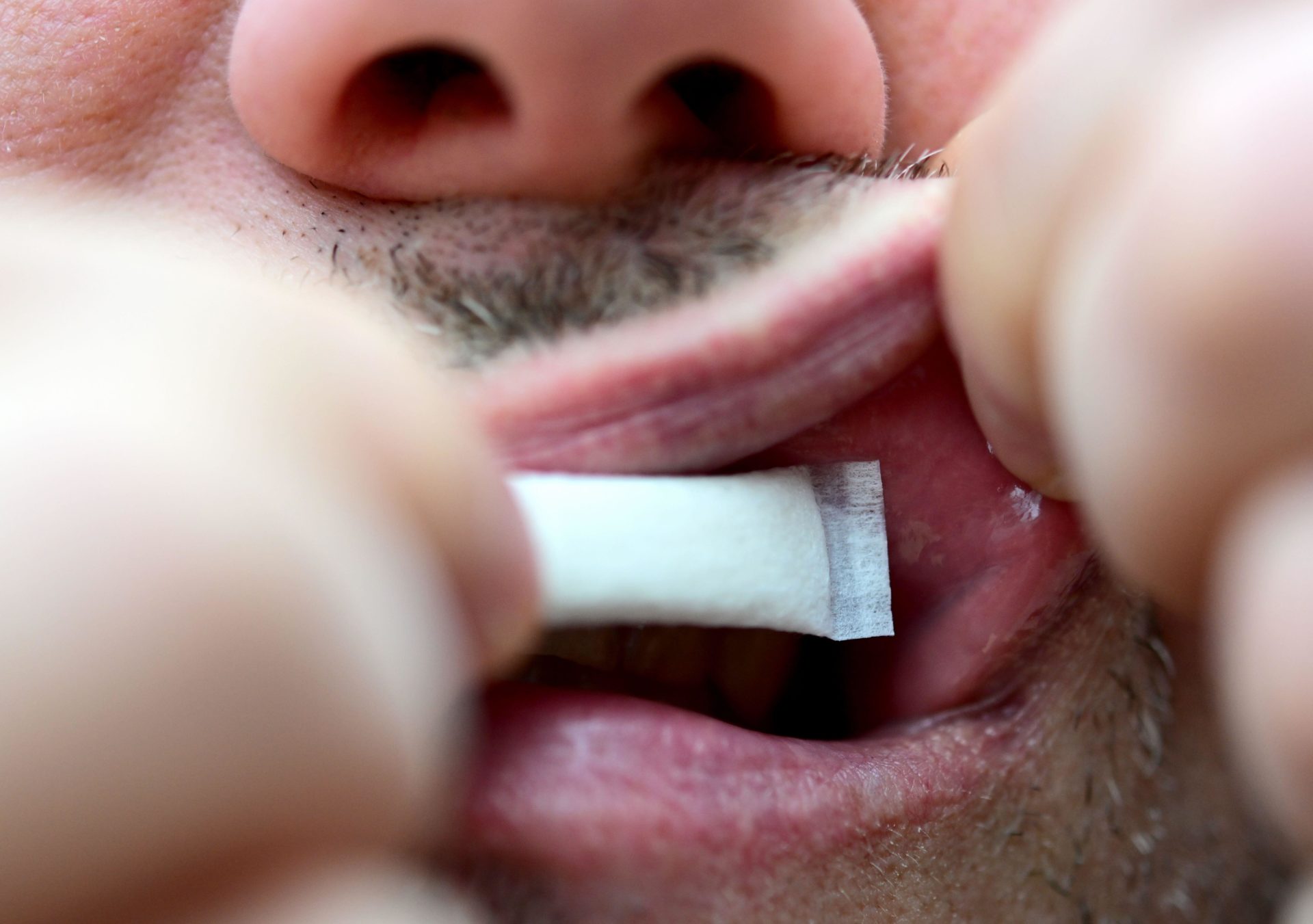 A person pushes a nicotine pouch under their upper lip.