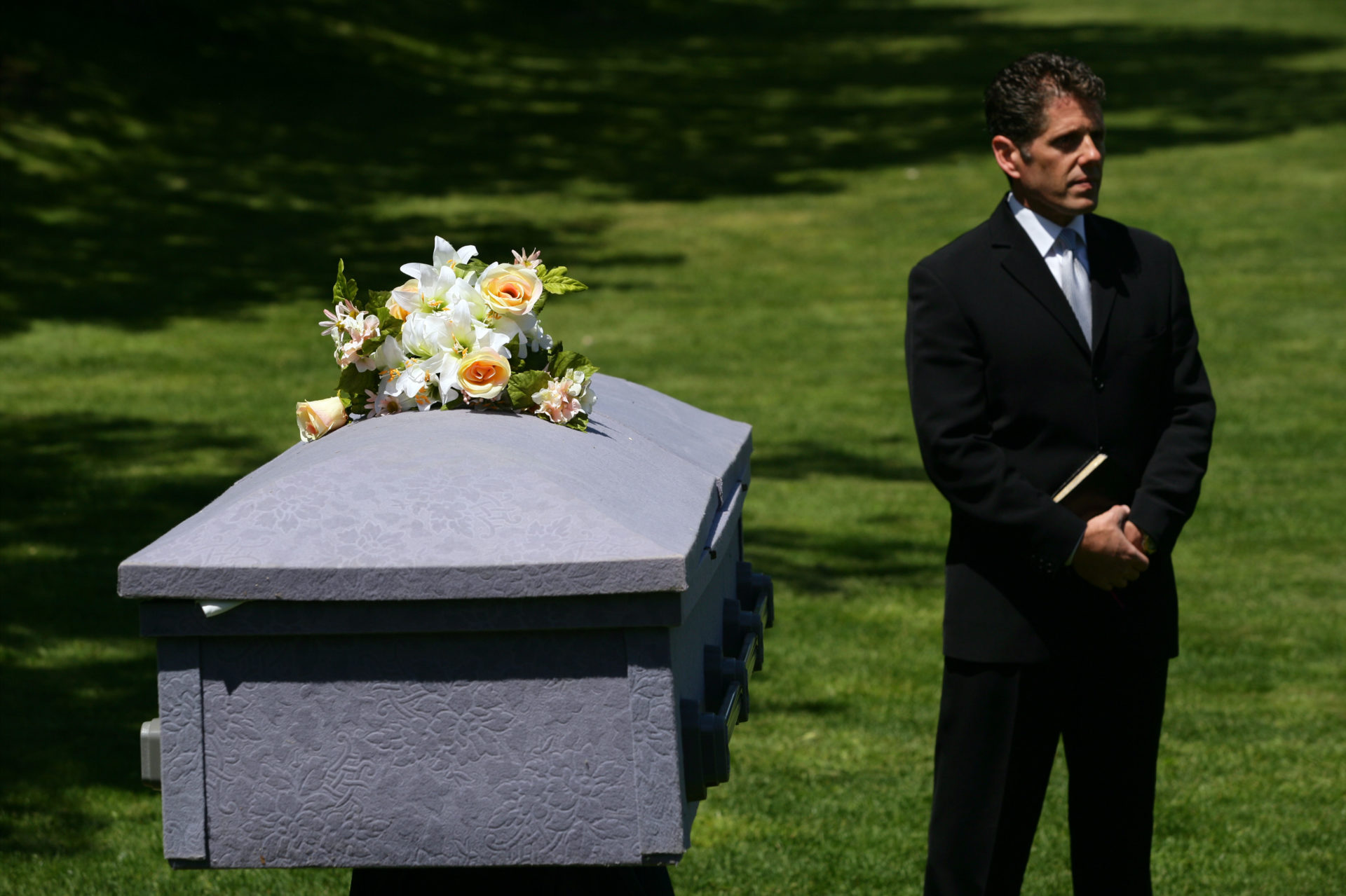 A man stands next to a coffin in a cemetery