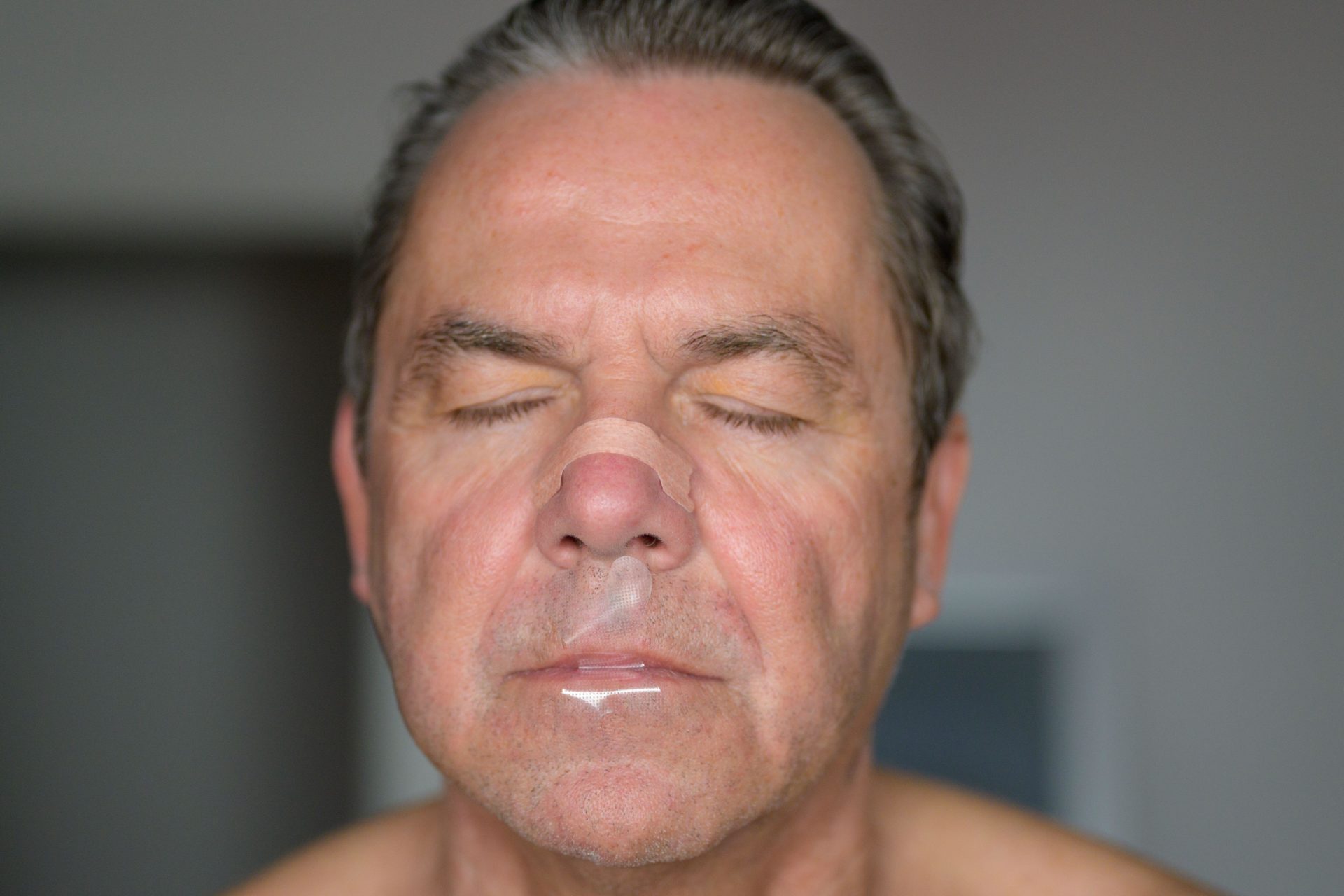 Close up of a middle aged man with a anti-snore nose strip and mouth tape on. Image: Alamy