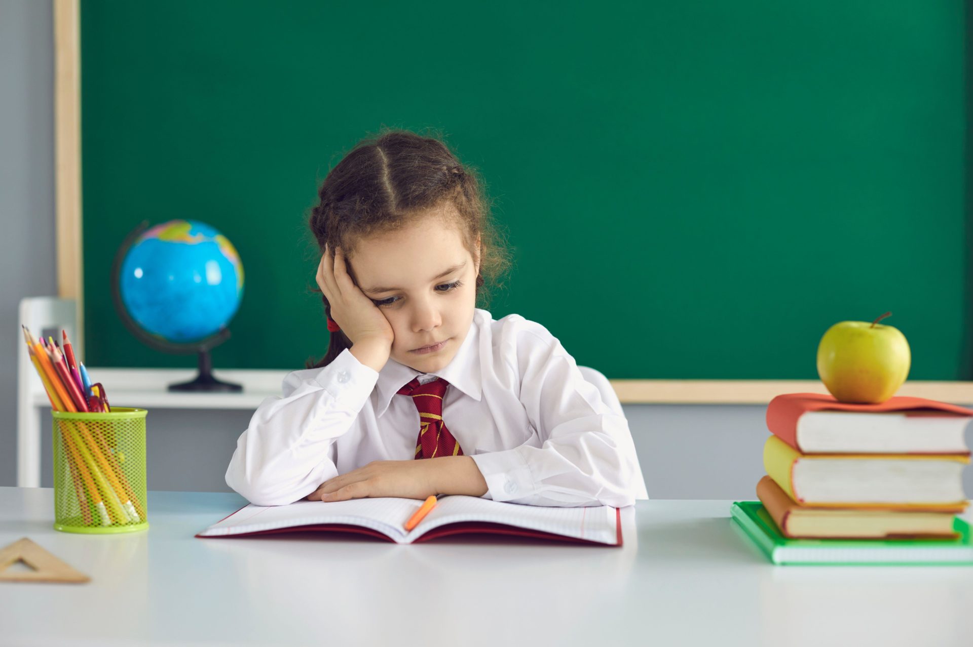 Sad schoolgirl looks at a book while sitting in class. A math problem in a child at school.