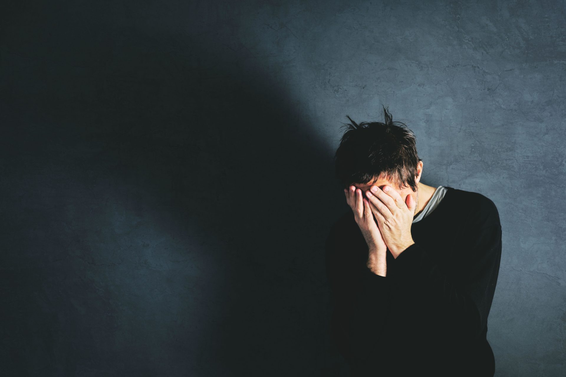 Grief concept, man coping with the loss in state of emotional distress, overwhelmed and helpless. Adult male covering face with his hands