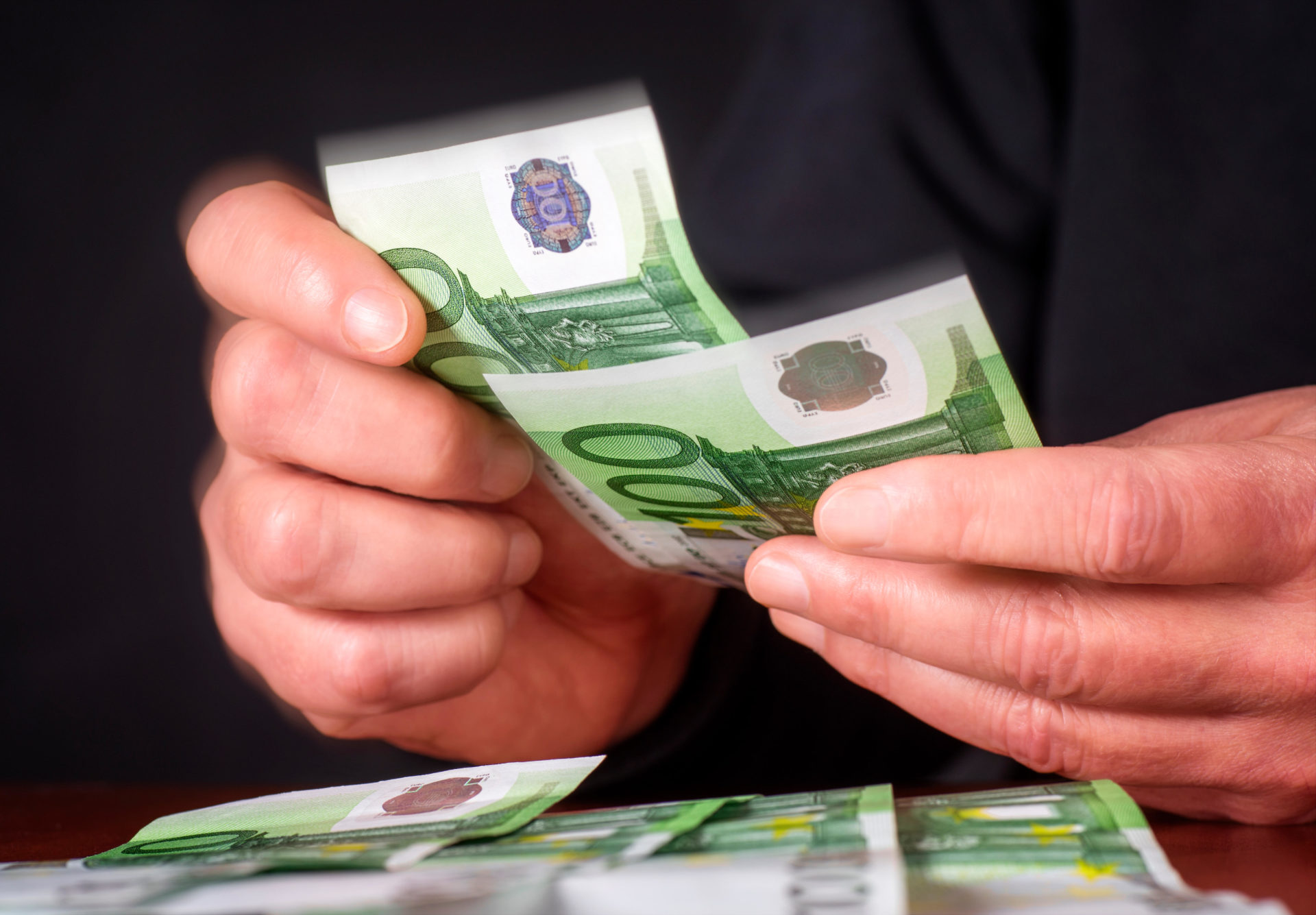 Hands with 100 Euro banknotes, which are counted and put on a table.