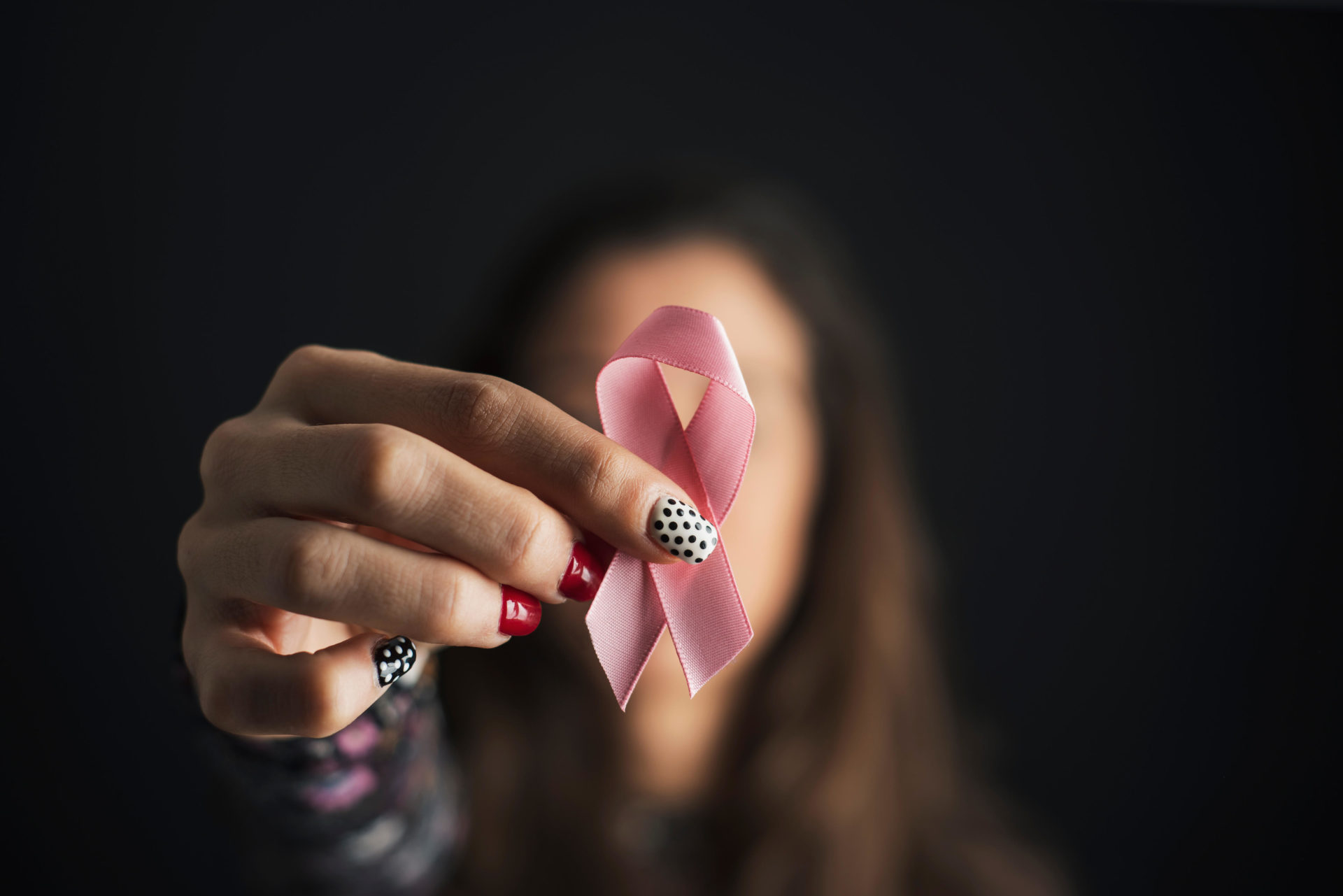 Closeup of a young caucasian woman holding a pink ribbon in front of her face for breast cancer awareness. Image: Alamy