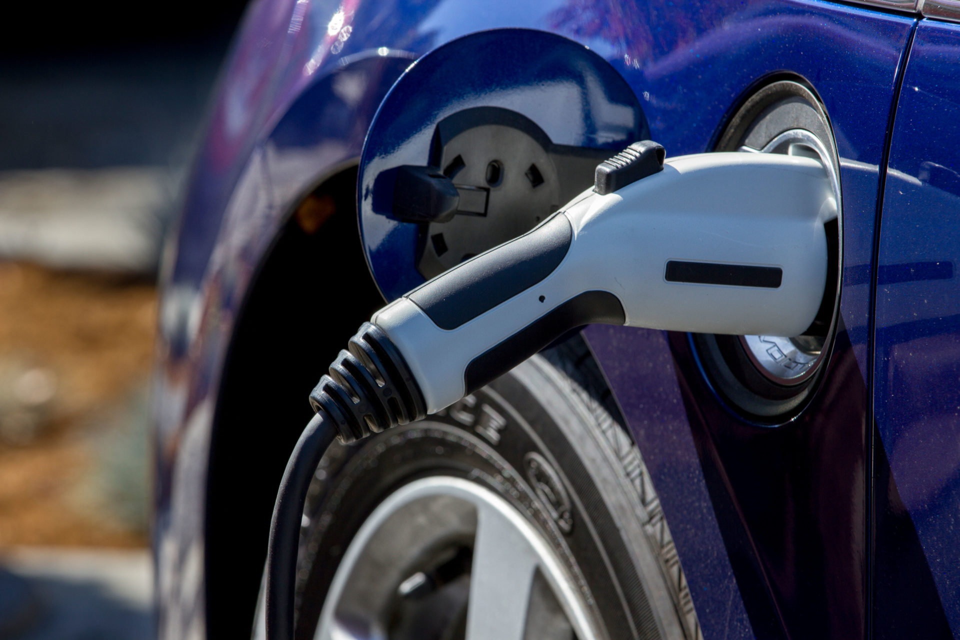 Blue plug-in electric car with connector plugged into a charging station to charge its battery in a company parking lot. Image: Alamy