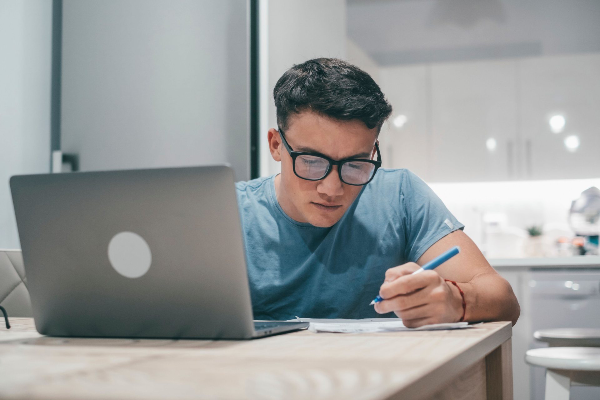 One young teenager studying and working at home at night on the table using laptop pc smiling and having fun doing homework.