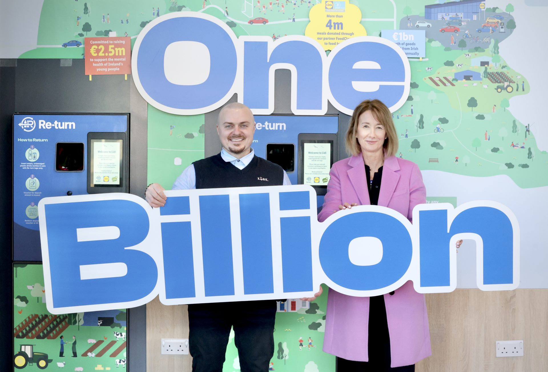 Two staff from Re-turn hold a sign saying 'One Billion' in front of return bottle machines