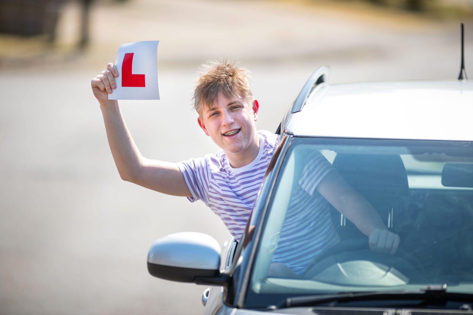 2BWGF20 Teenager learner driver celebrating passing his driving test waving his L plates in the air.