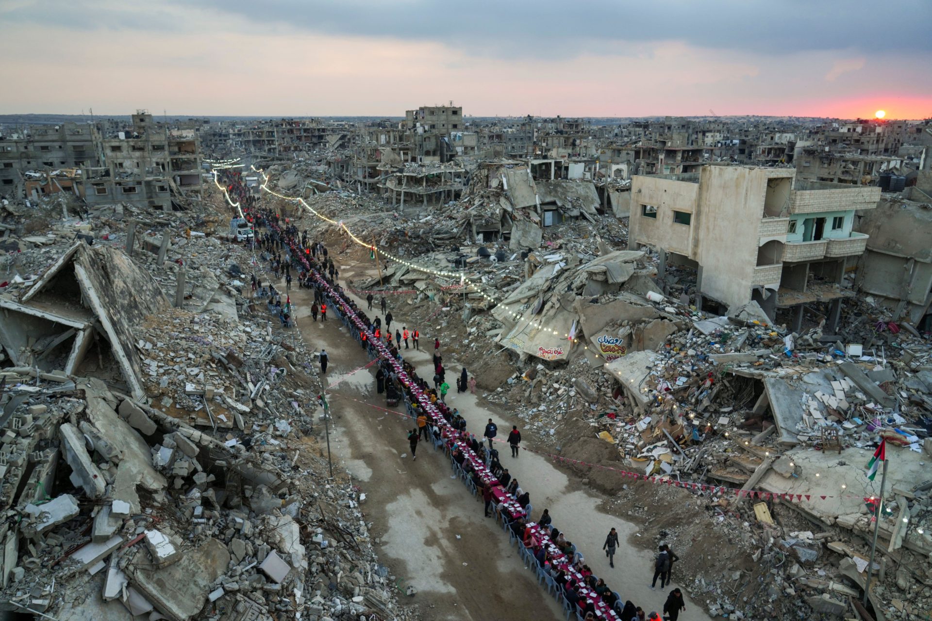 As the sun sets, Palestinians sit at a large table surrounded by the rubble of destroyed homes and buildings as they gather for iftar, the fast-breaking meal, on the first day of Ramadan in Rafah.