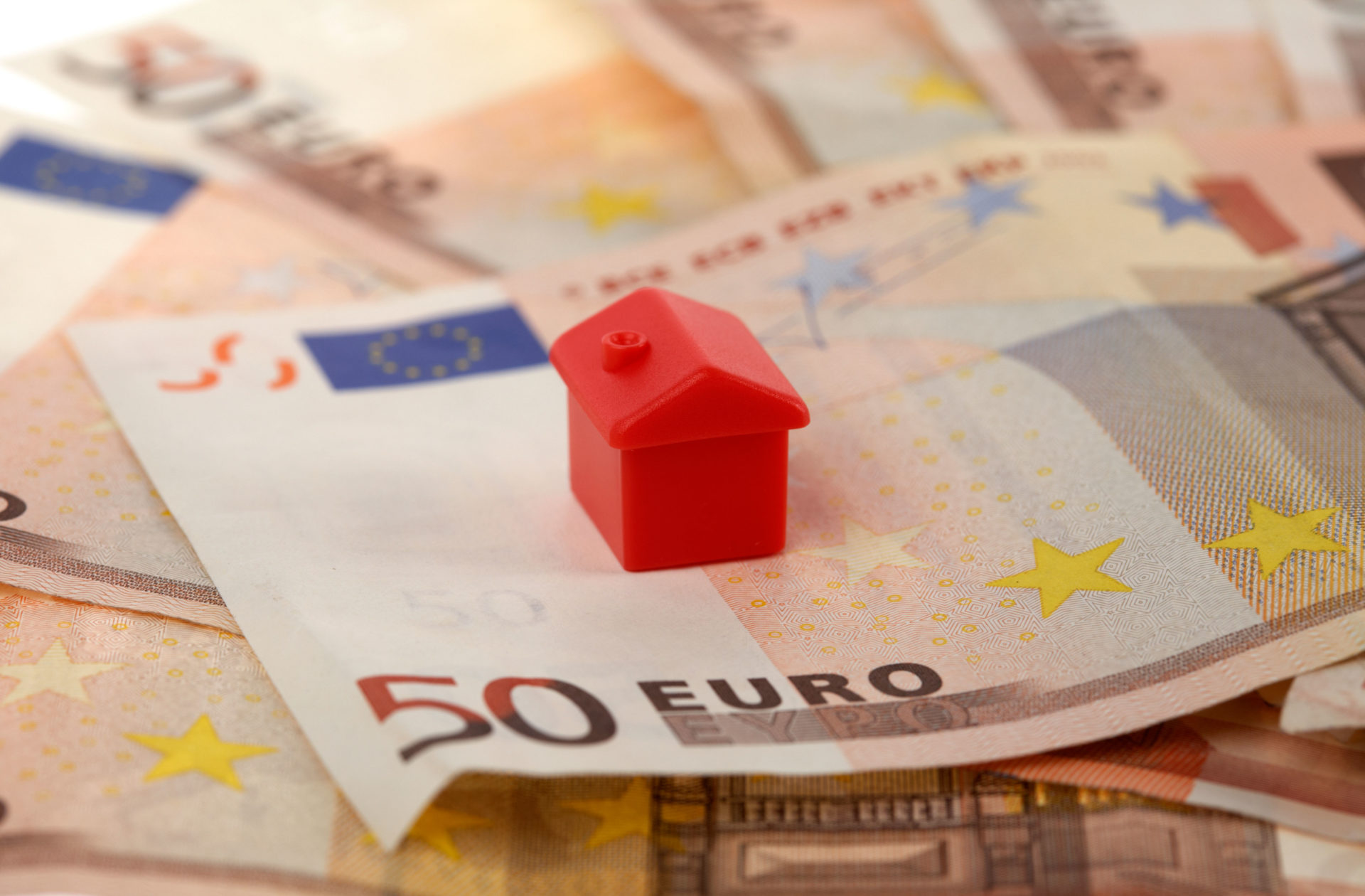 One red house on top of a pile of 50 euro bank notes cash. Image: Alamy