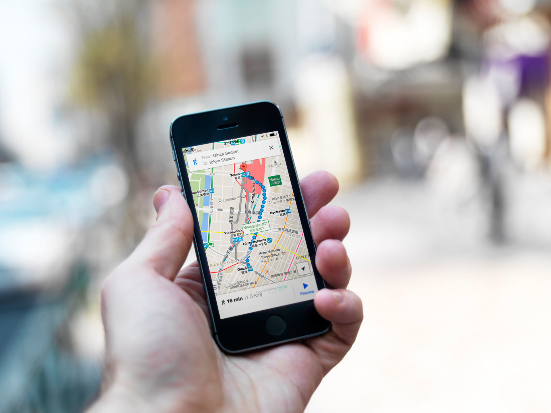 Person hand with iPhone displaying Google maps GPS navigator on streets of Tokyo, Japan.
