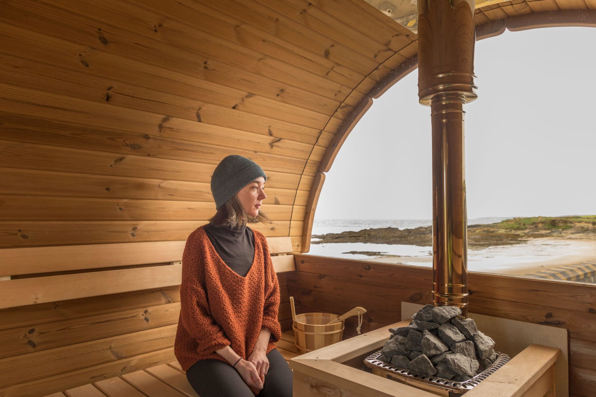 Woman sits in her new mobile wood burning sauna on the seafront at Garrettstown, Co. Cork, Ireland.