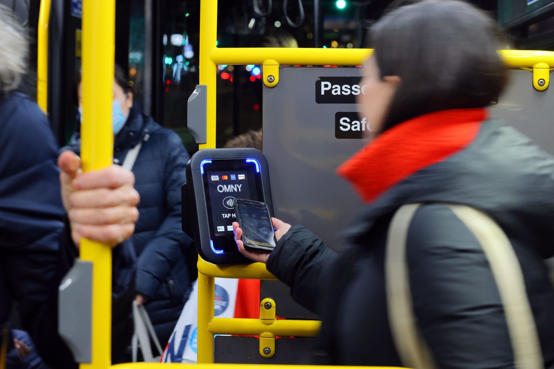 A person taps a smartphone to an OMNY contactless payment reader on a NYC Transit bus.