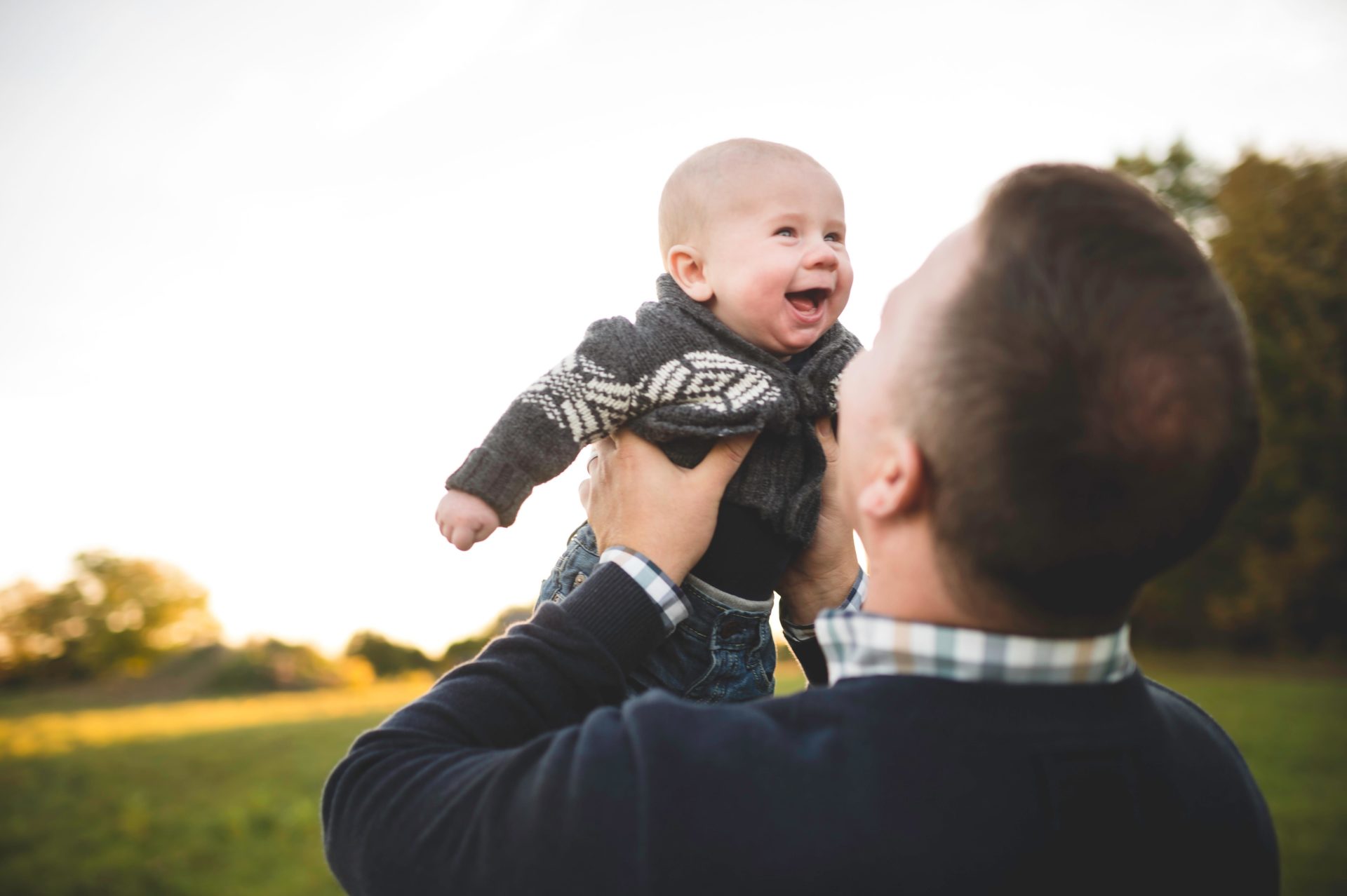 Man holding up baby son in field.