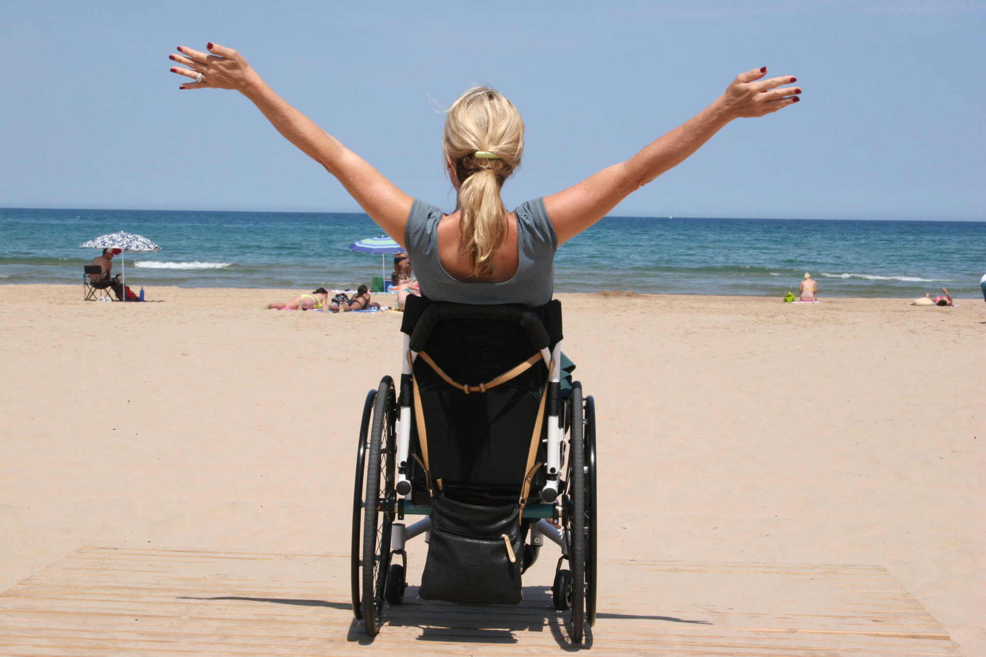 Woman in a wheelchair with her arms outstretched on a beach looking at the ocean.
