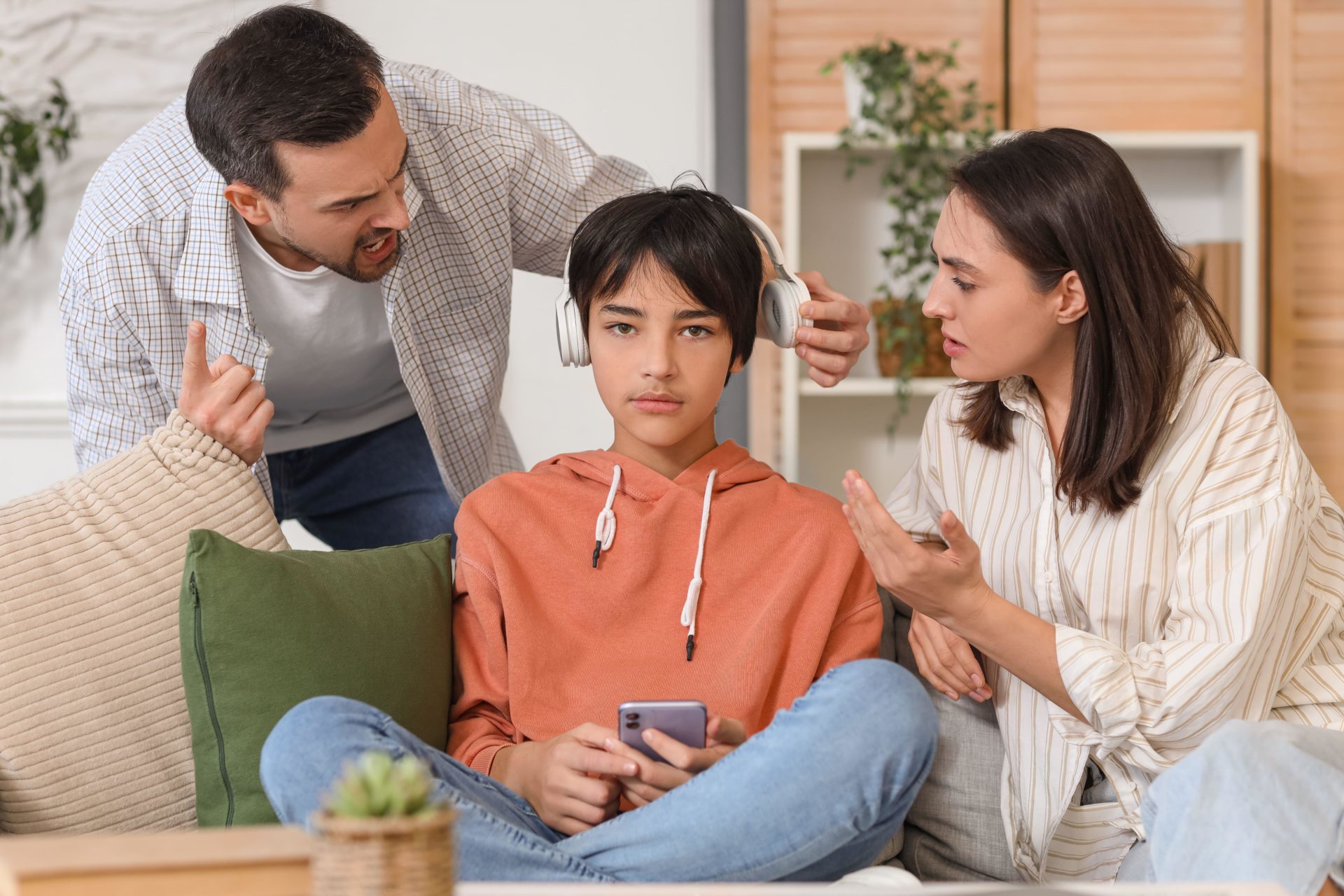 Angry parents arguing with their teenage son in headphones at home.
