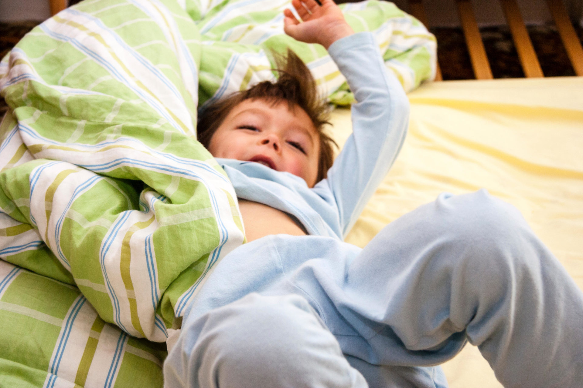 Boy, 4-5 year old, wearing blue pyjamas, laying on bed and throwing himself about with the duvet during a temper tantrum.